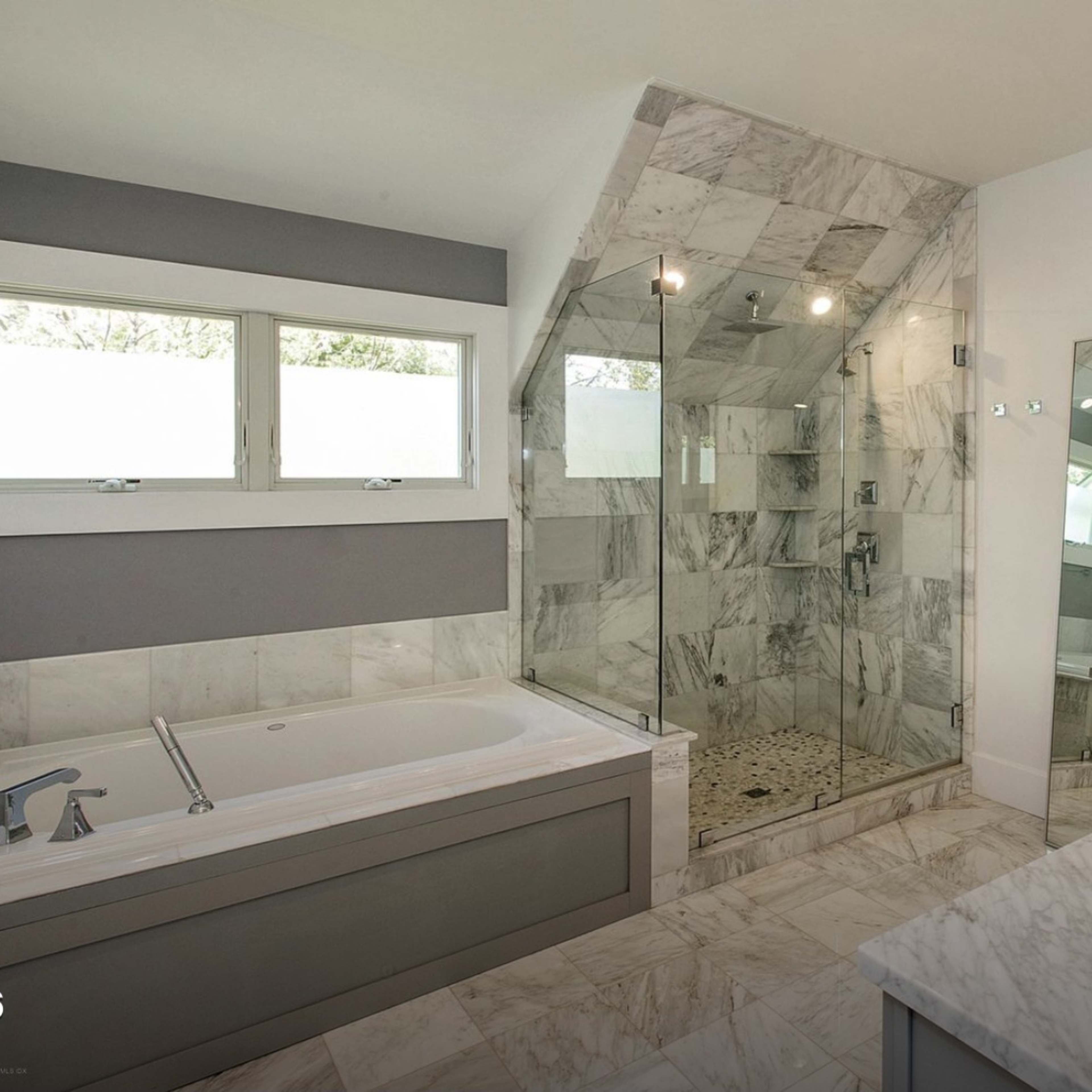 A modern bathroom featuring a glass shower, a freestanding tub, double sinks, and marble tile throughout.