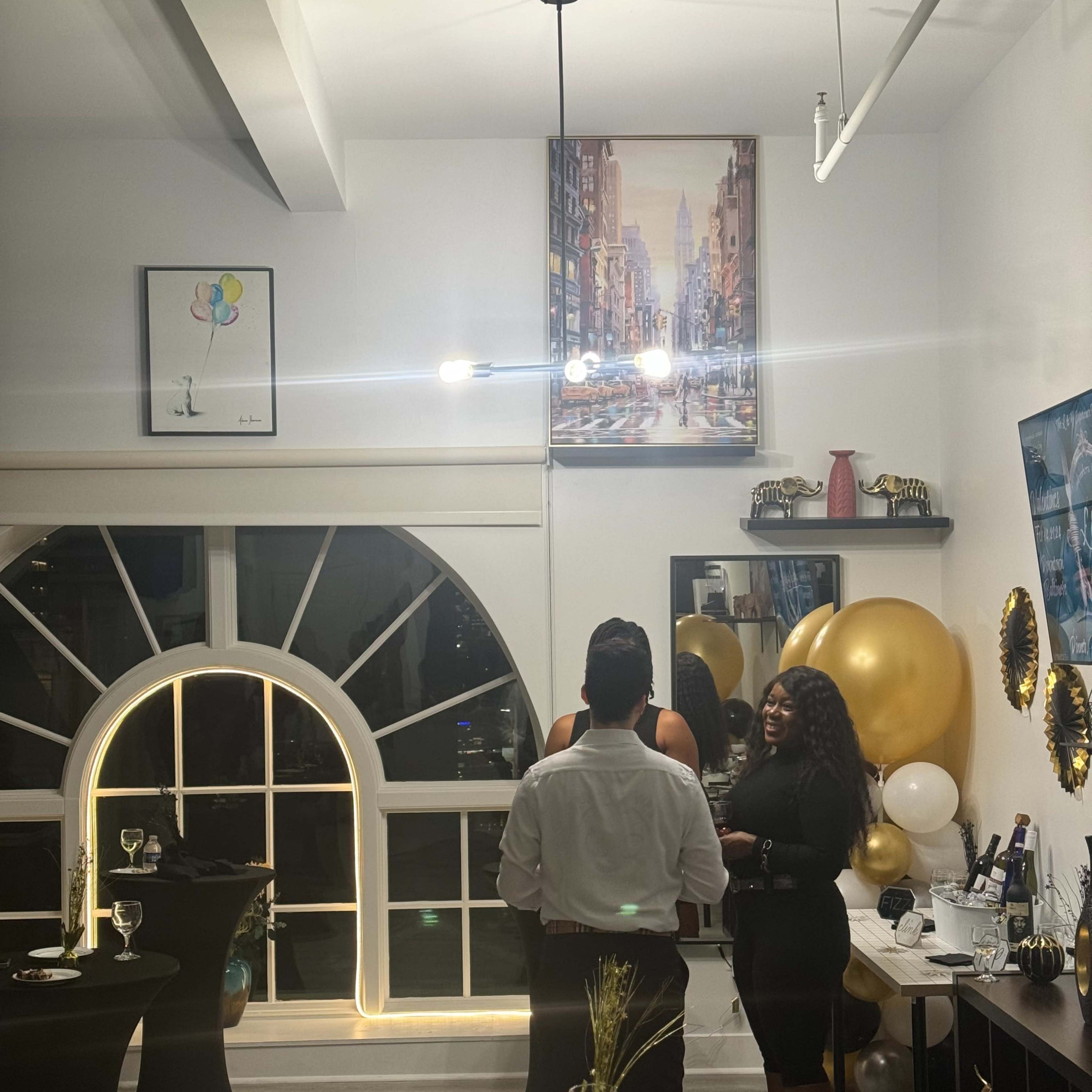 A man and a woman converse in a decorated event space featuring balloons, elegant furniture, and artwork on the walls.