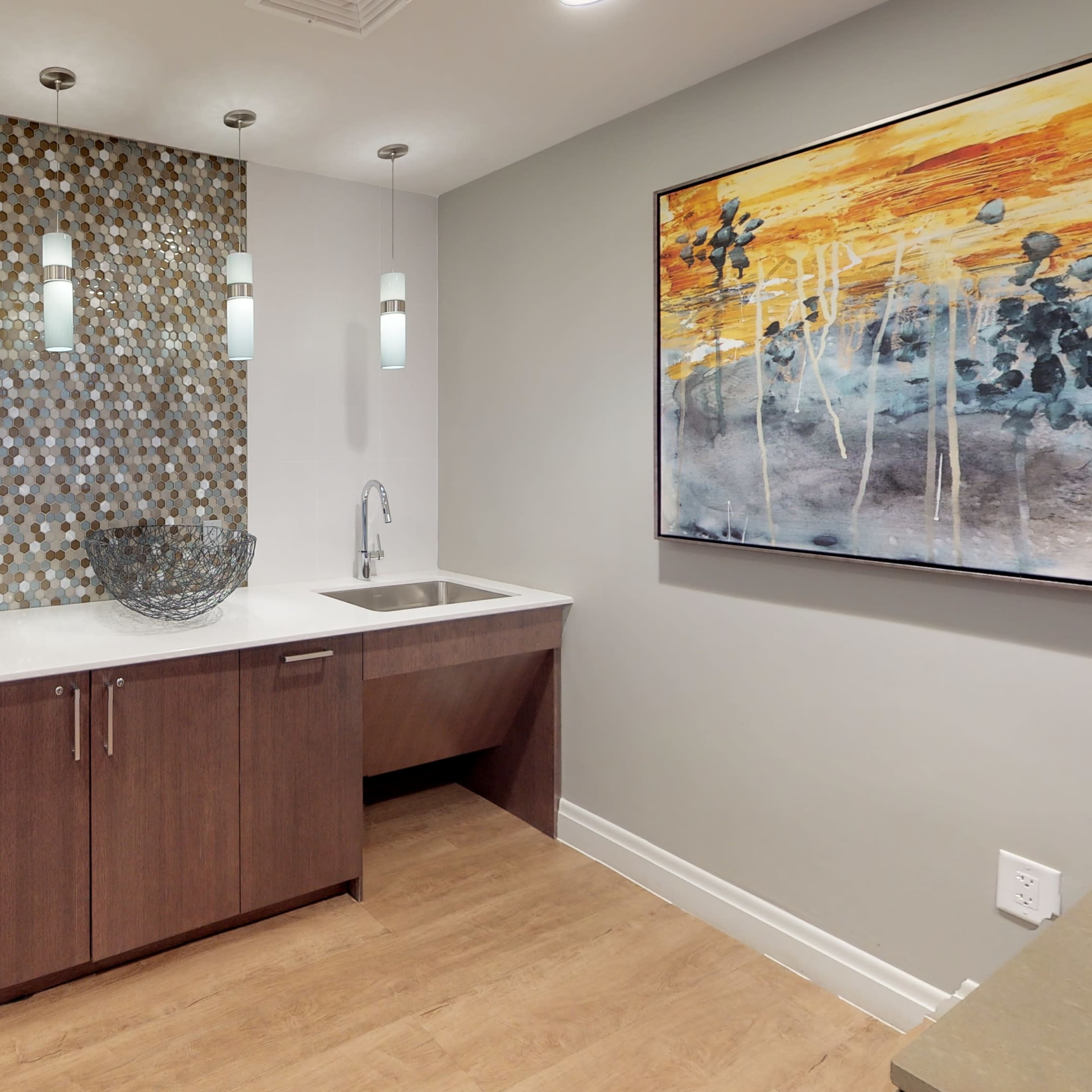 A modern kitchenette features a wooden cabinet below a minimalist countertop with a sink, decorative items, and a mosaic wall.