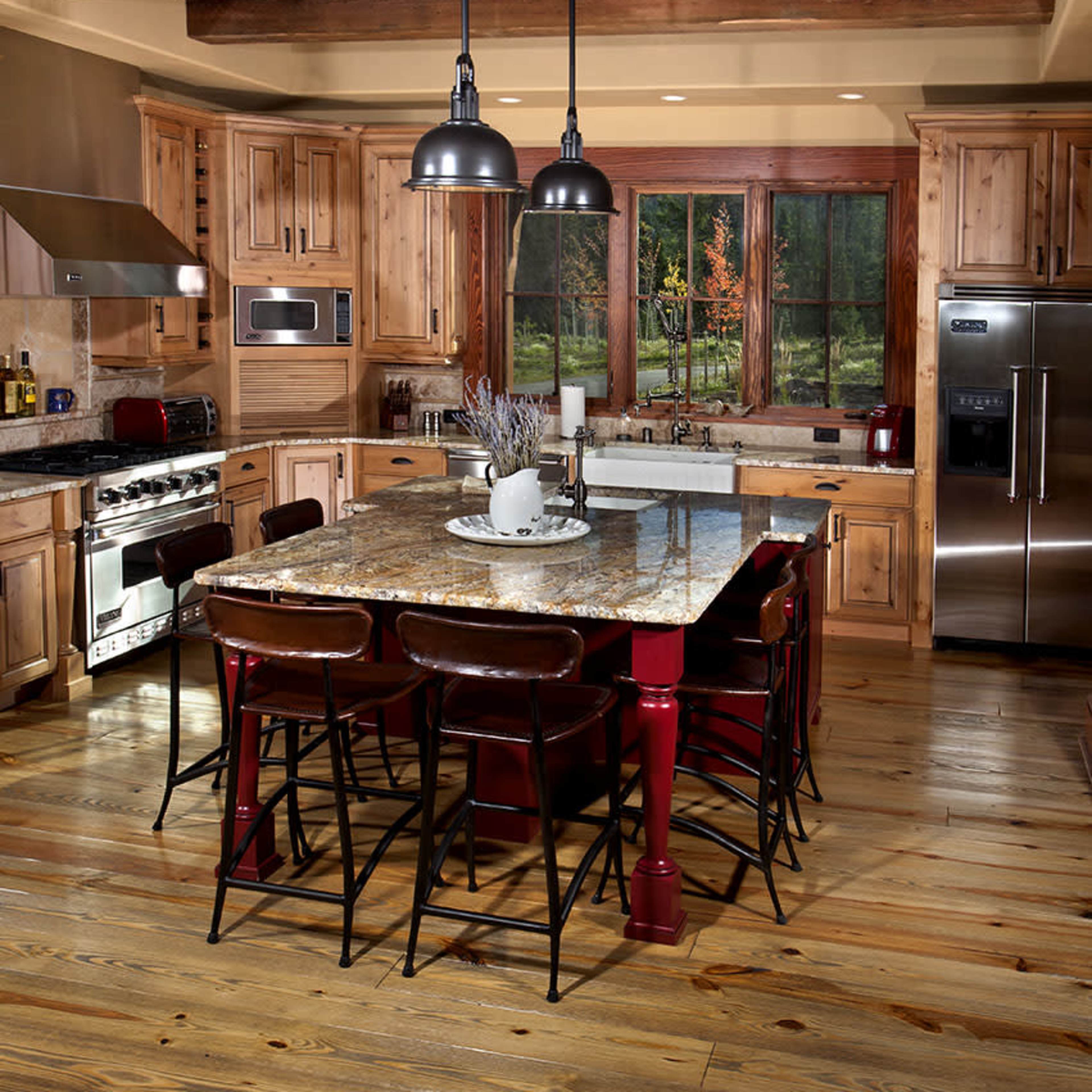 A spacious kitchen features a large granite island surrounded by barstools, wooden cabinets, and stainless steel appliances.