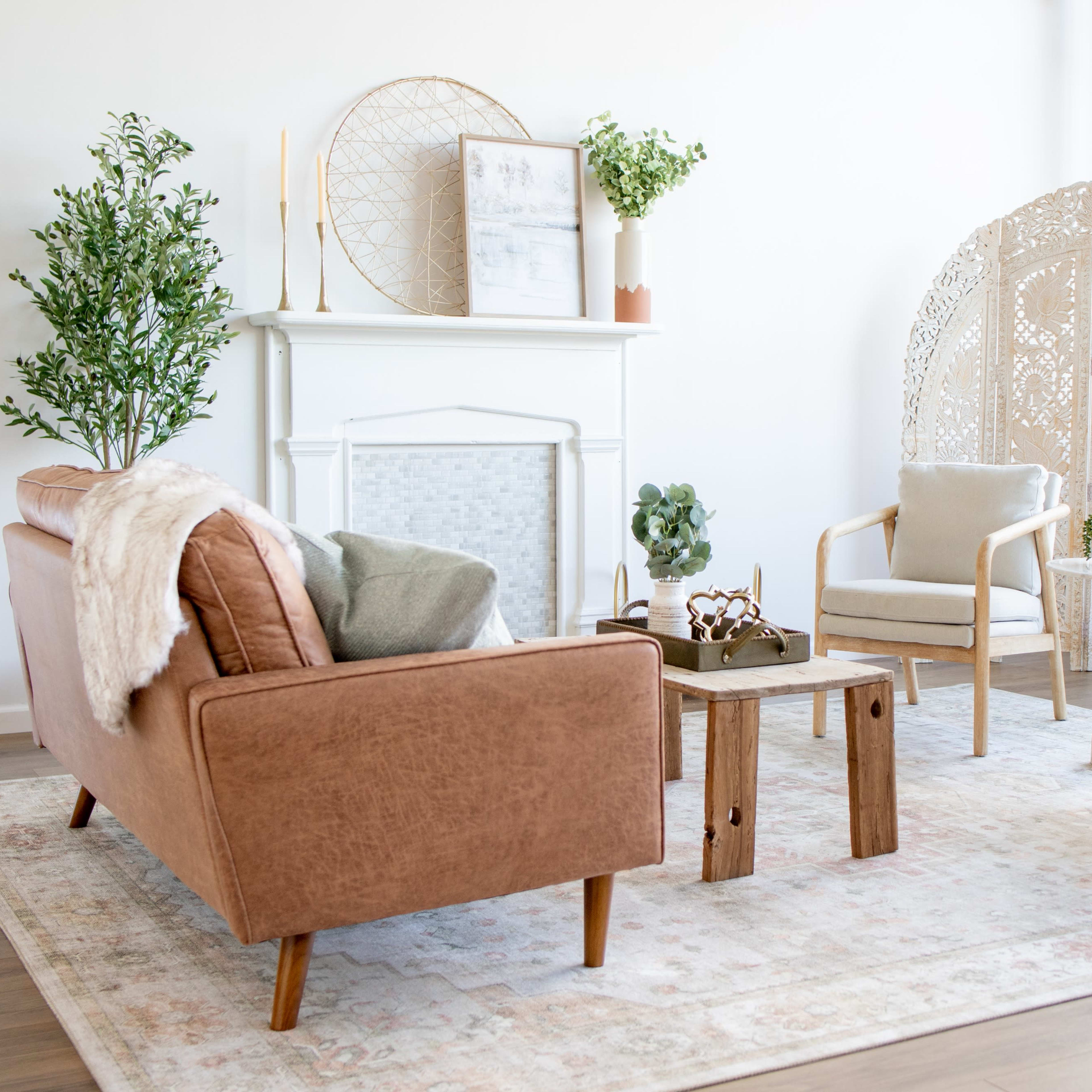 A bright, modern living room featuring a brown sofa, light-colored armchairs, a small wooden coffee table, and decorative plants.