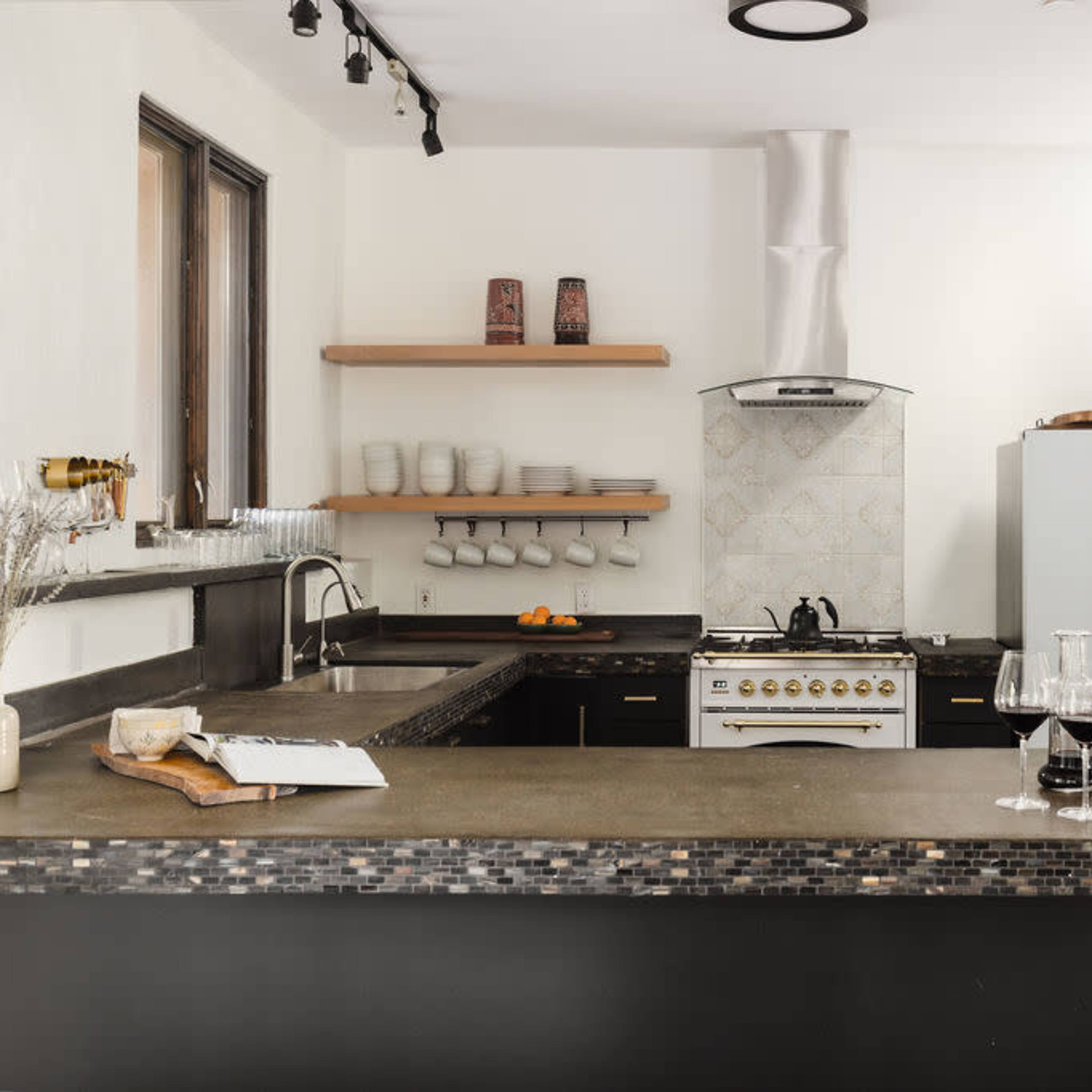 A modern kitchen features a large island with a dark countertop, white cabinets, a stainless steel refrigerator, and an elegant stove against a patterned backsplash.