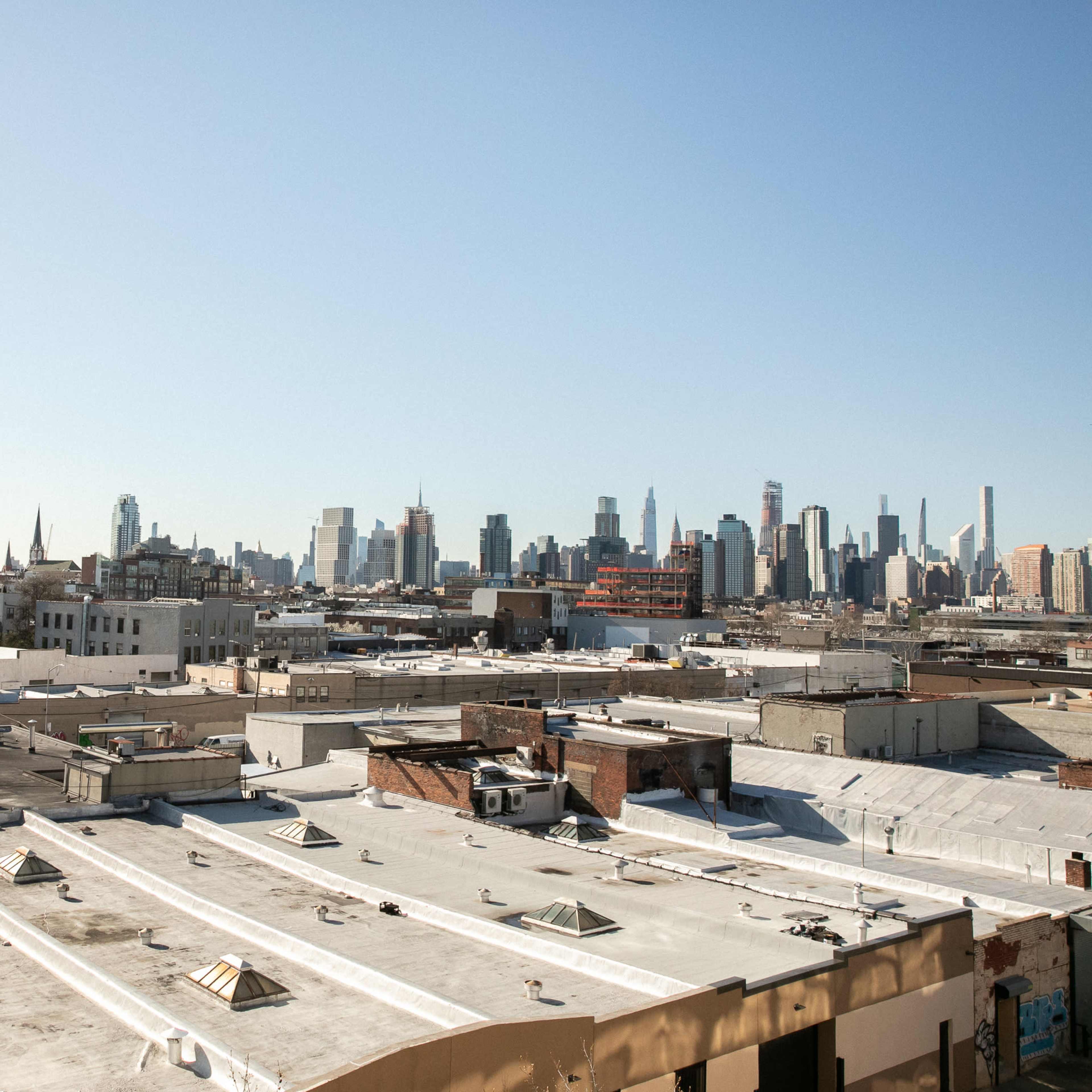 A panoramic view of a city skyline featuring various buildings and rooftops under a clear blue sky.