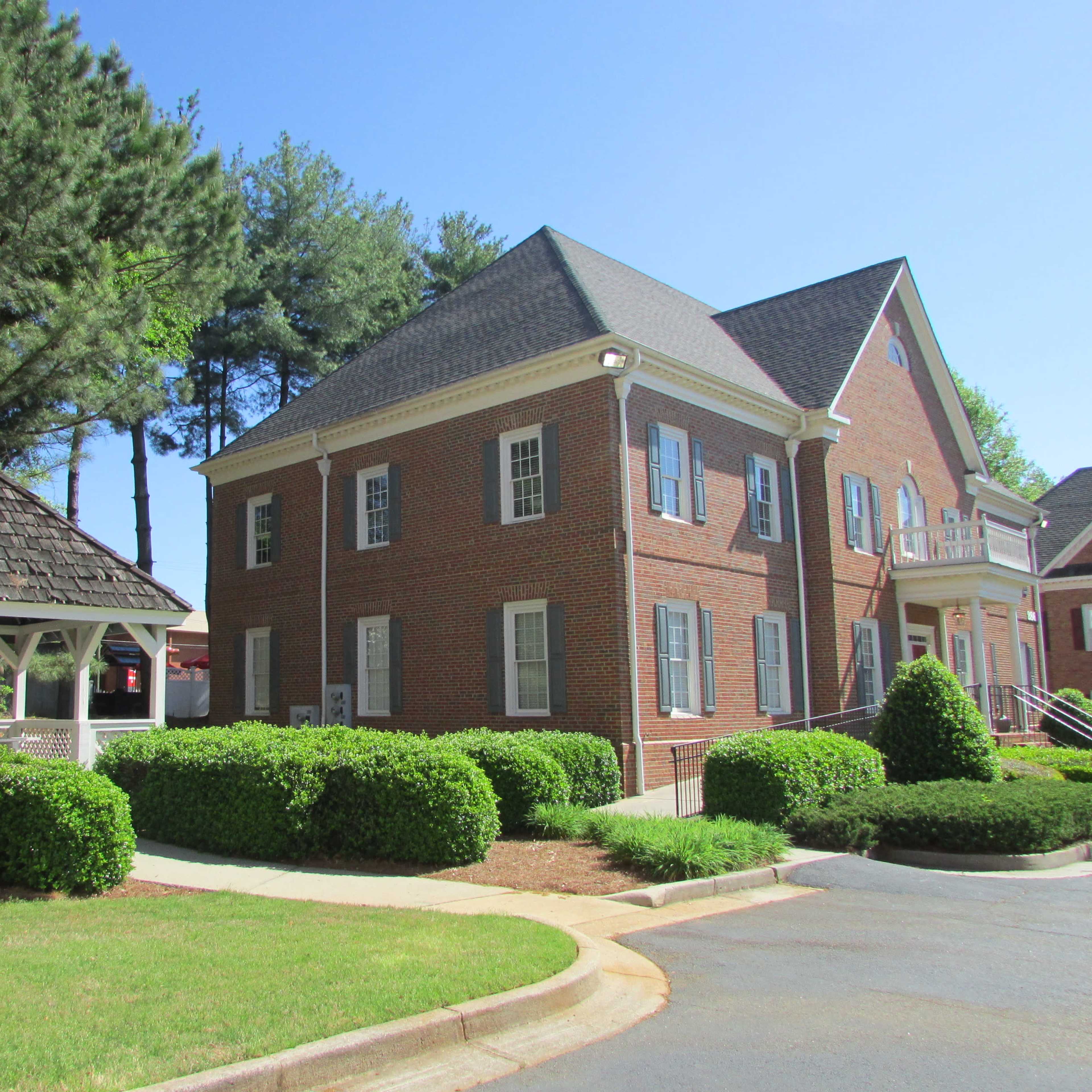 A brick building next to a gazebo surrounded by neatly trimmed shrubs and trees.