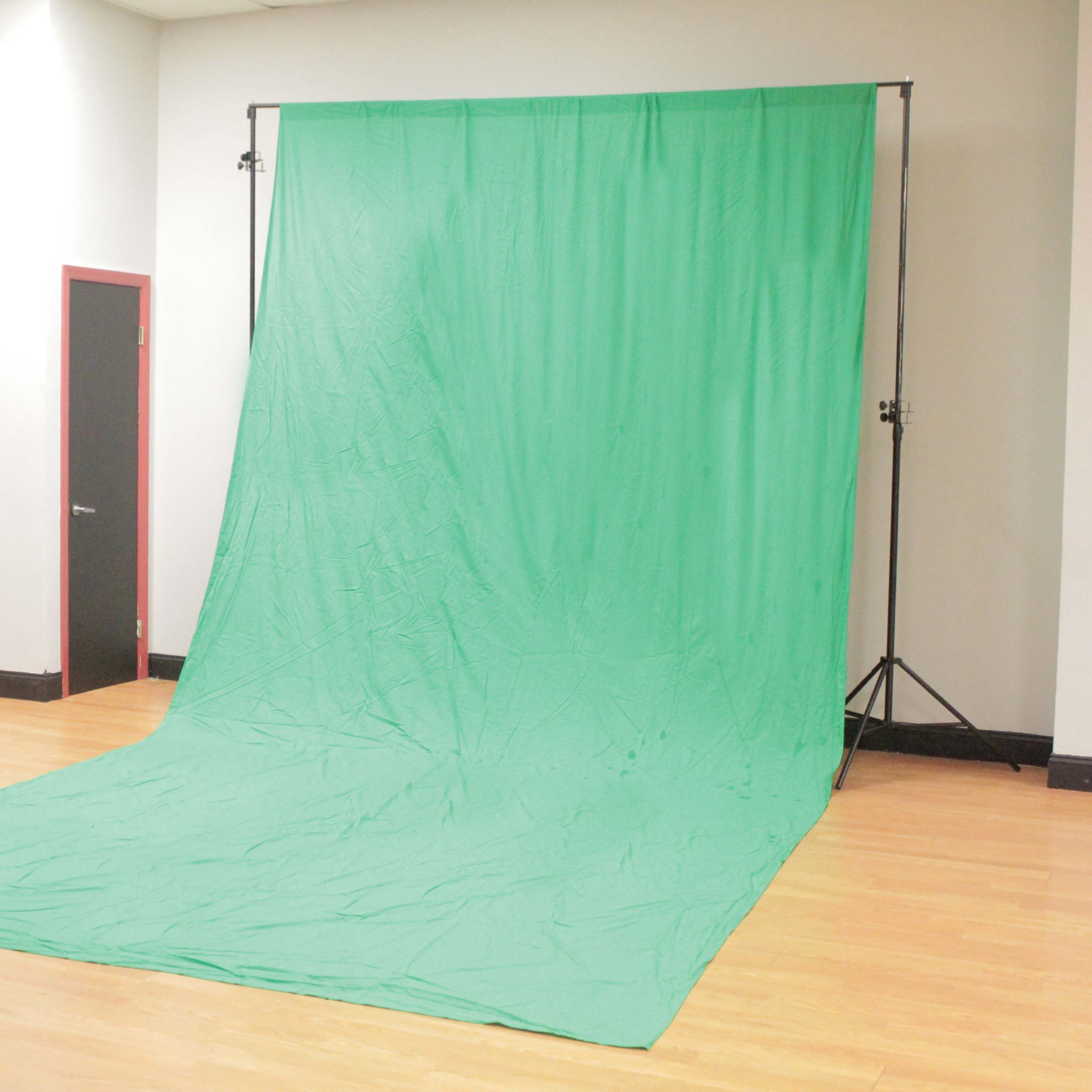 A green backdrop set up in a room with wooden flooring and plain walls.