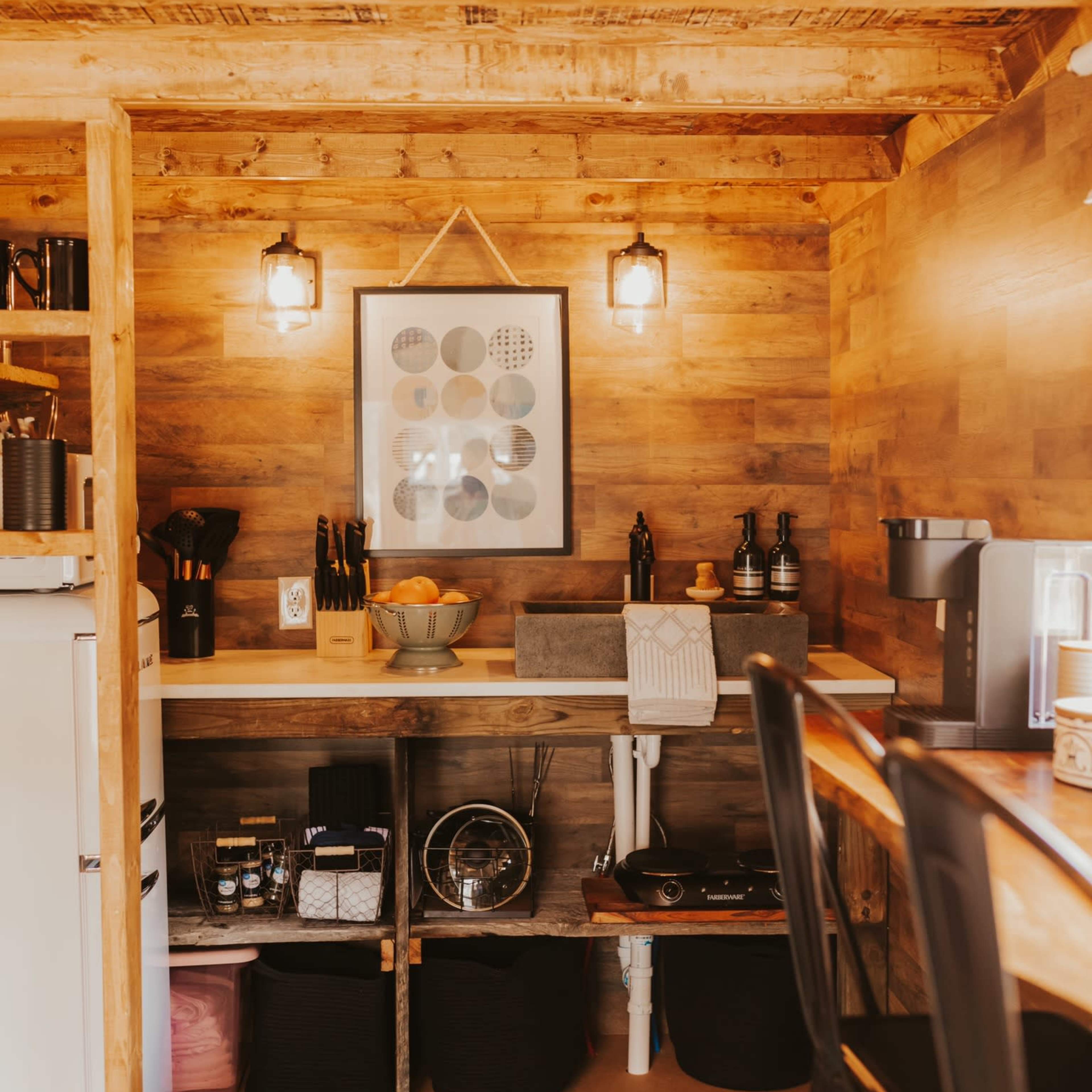 A small kitchen area with wooden walls and a countertop featuring various kitchen items, including a fruit bowl and kitchen appliances.
