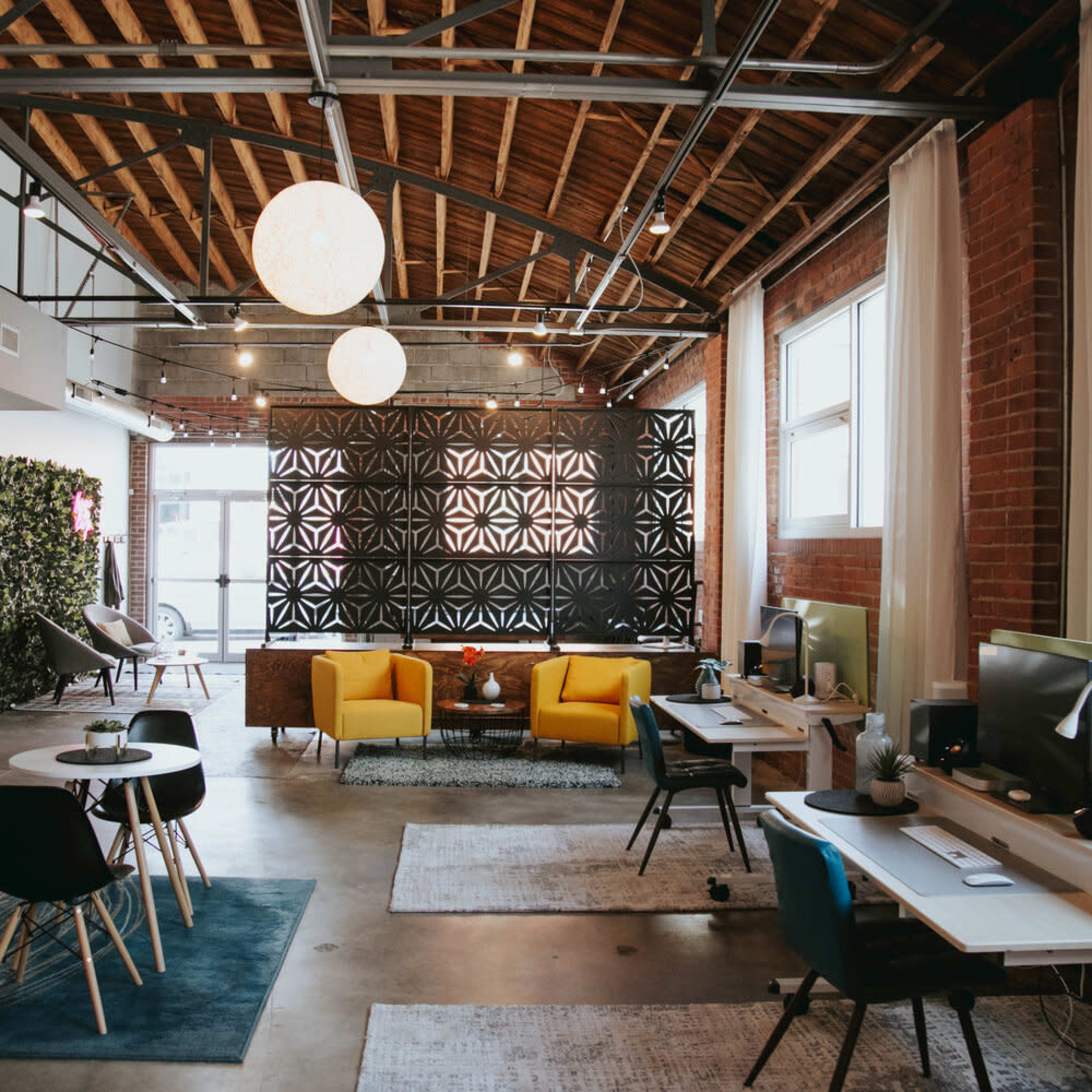 A modern open office space featuring yellow armchairs, a wall with decorative black panels, and multiple workstations with computers.