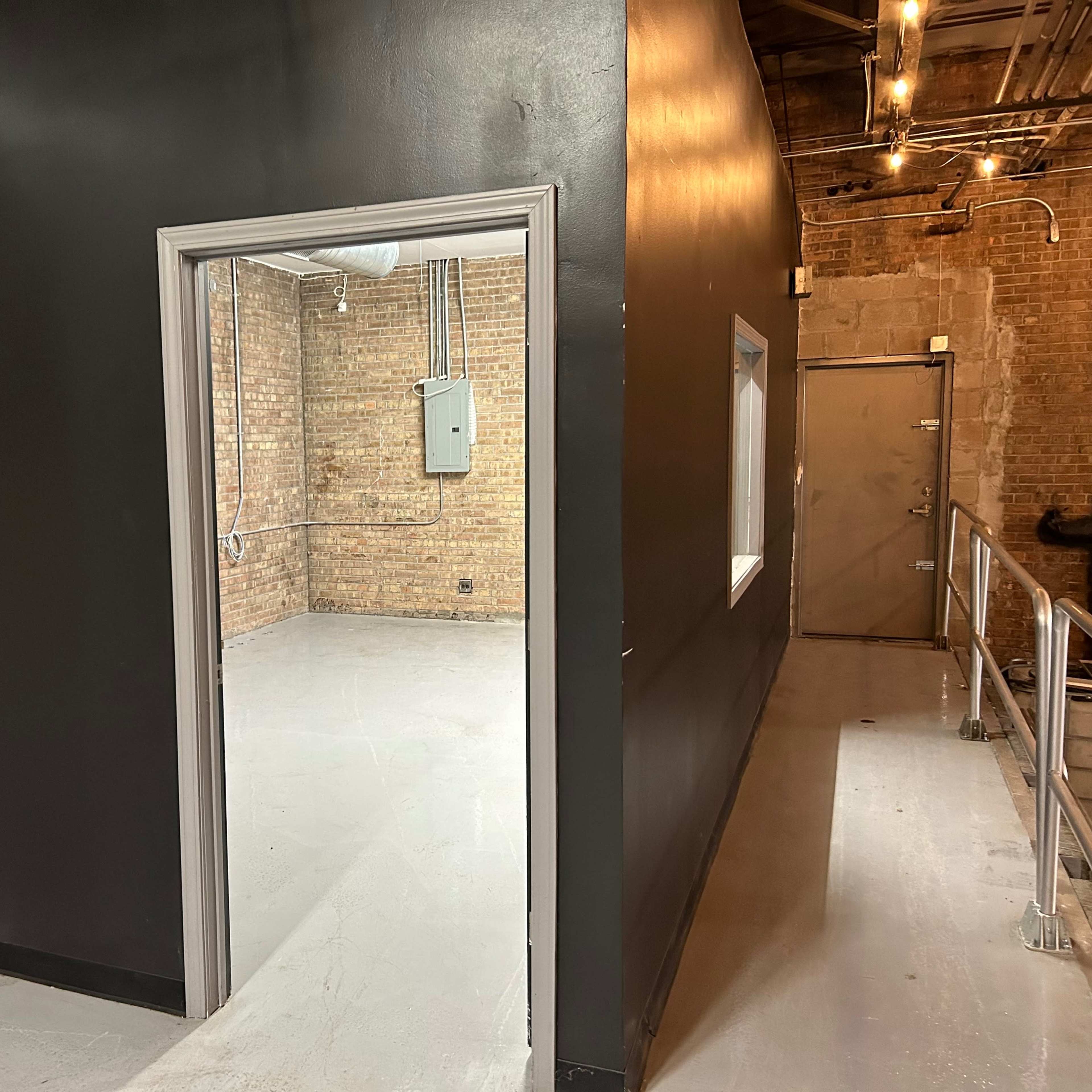 A doorway leading from a black-painted wall into a room with exposed brick walls and a concrete floor.