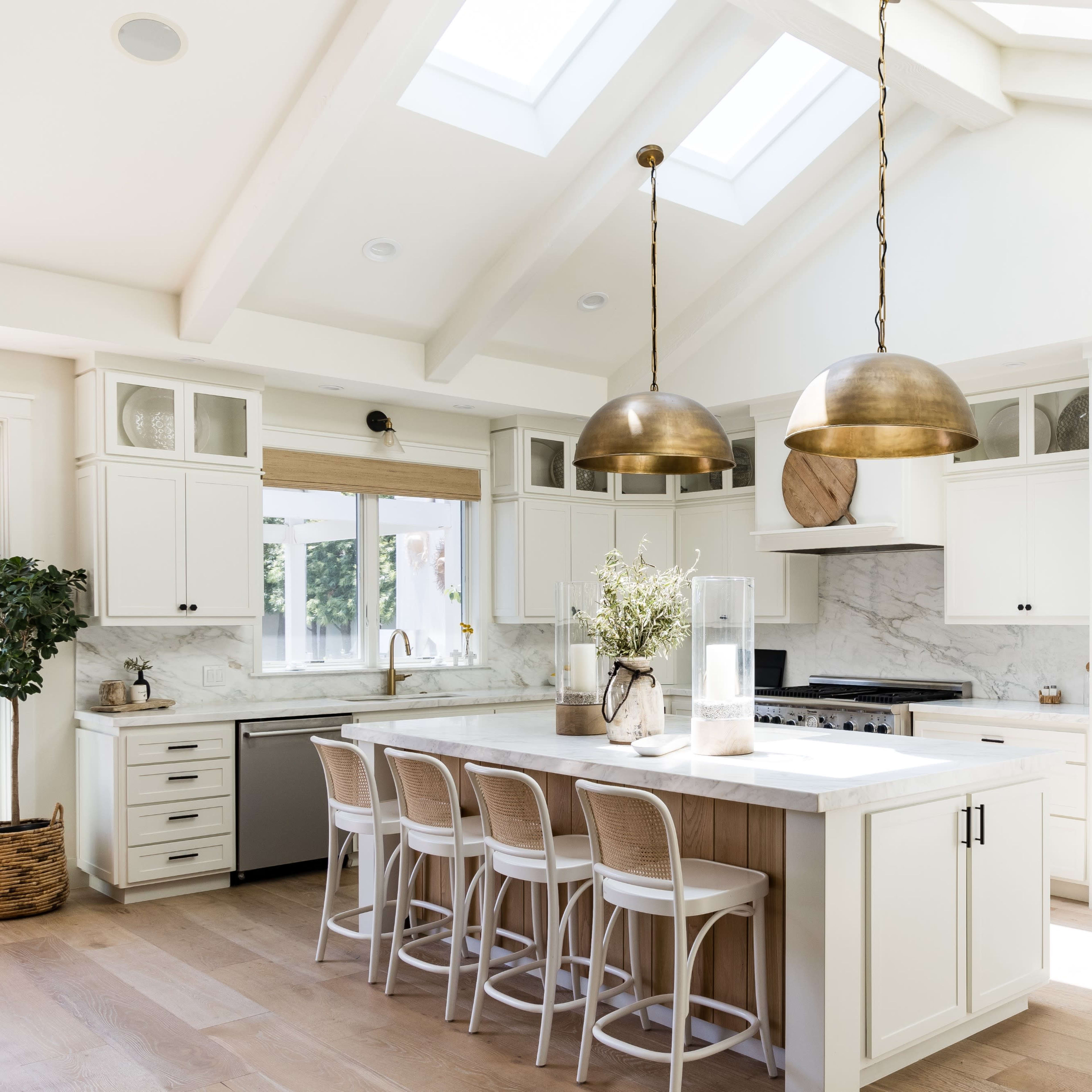 The kitchen features white cabinetry, a large island with seating, and skylights illuminating the space.