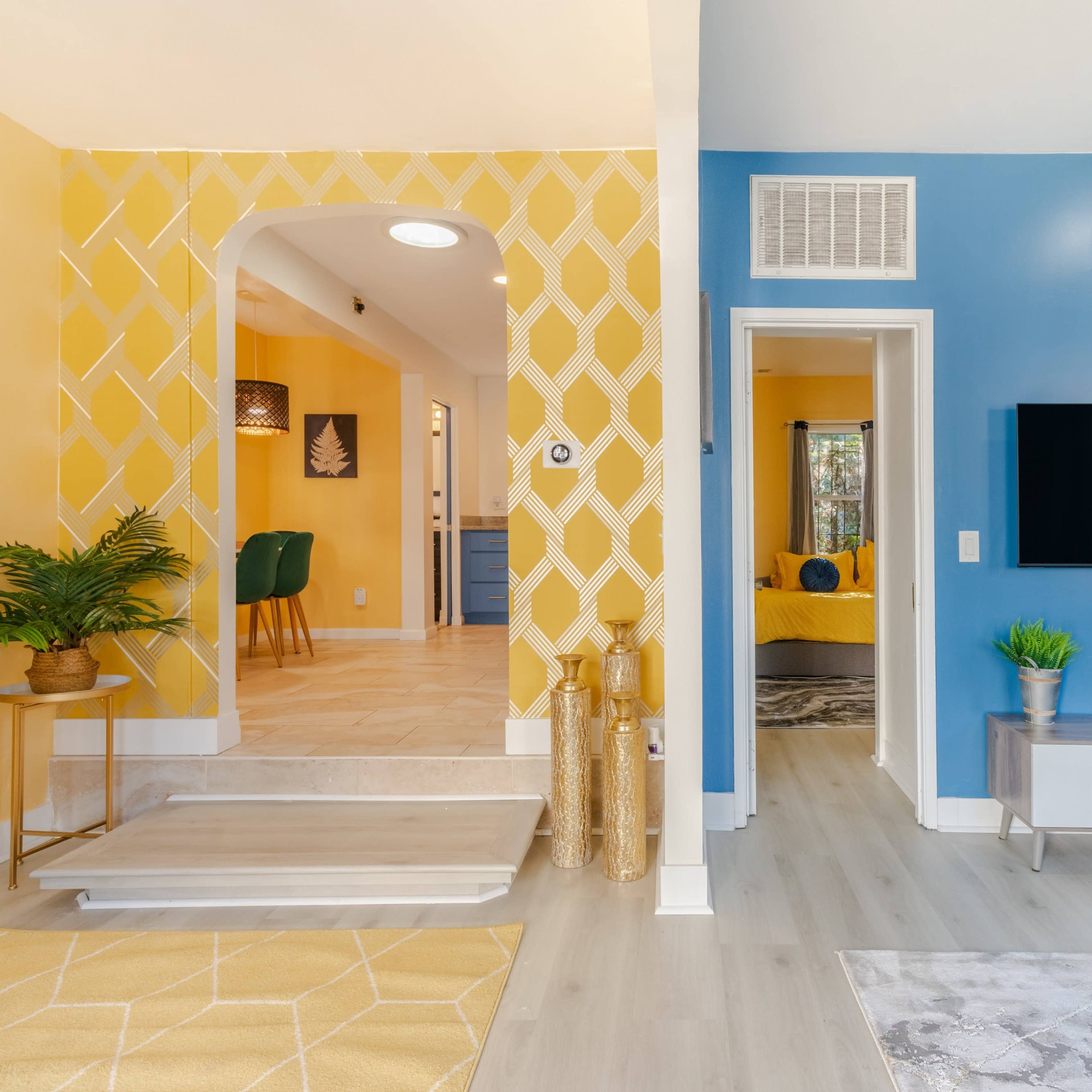 A bright, modern interior with contrasting yellow and blue walls, featuring an inviting living space and a visible hallway leading to another room.