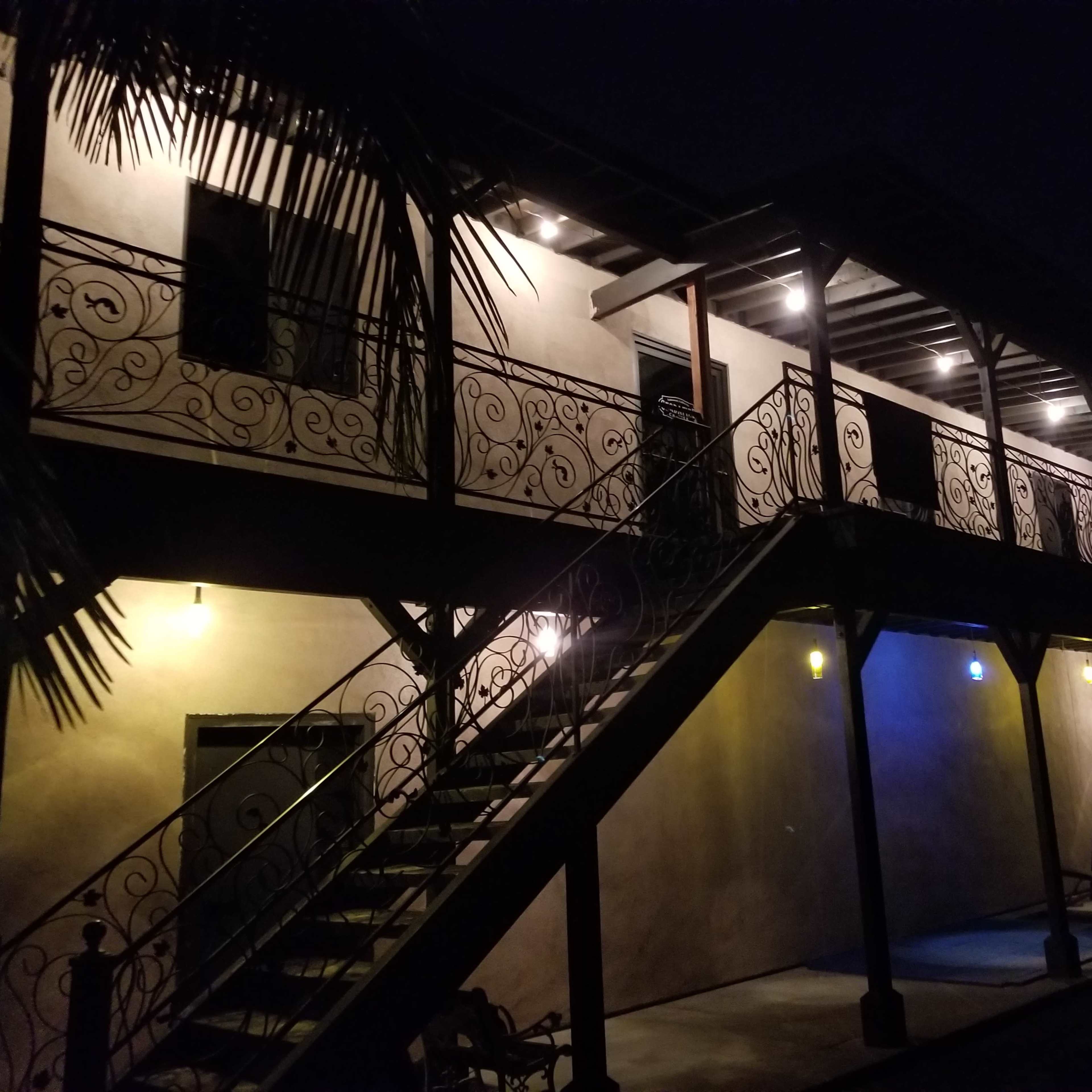 A two-story building with a staircase and decorative balcony lighting illuminates the exterior at night.