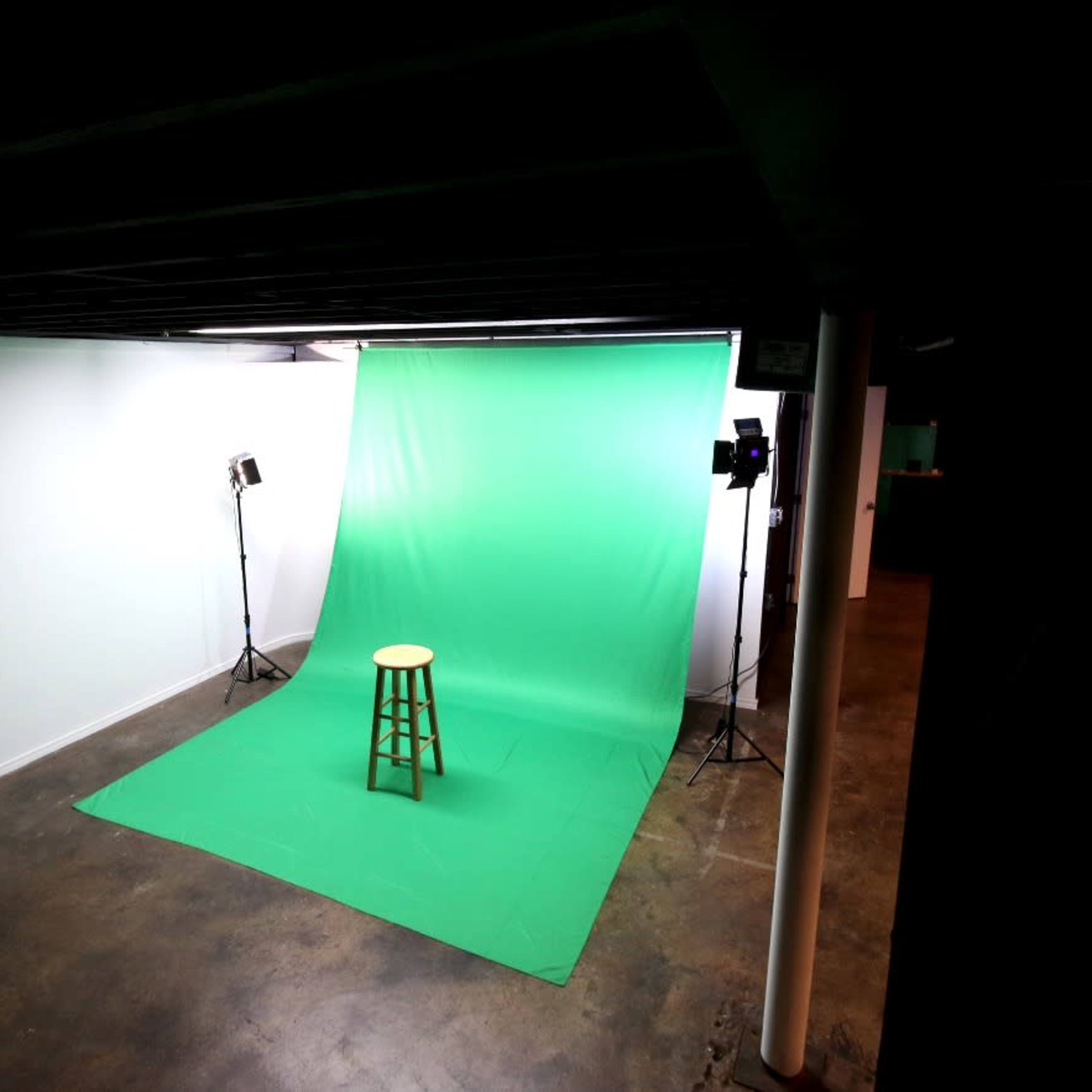A studio setup with a green backdrop, a wooden stool in front, and two lights positioned on either side.