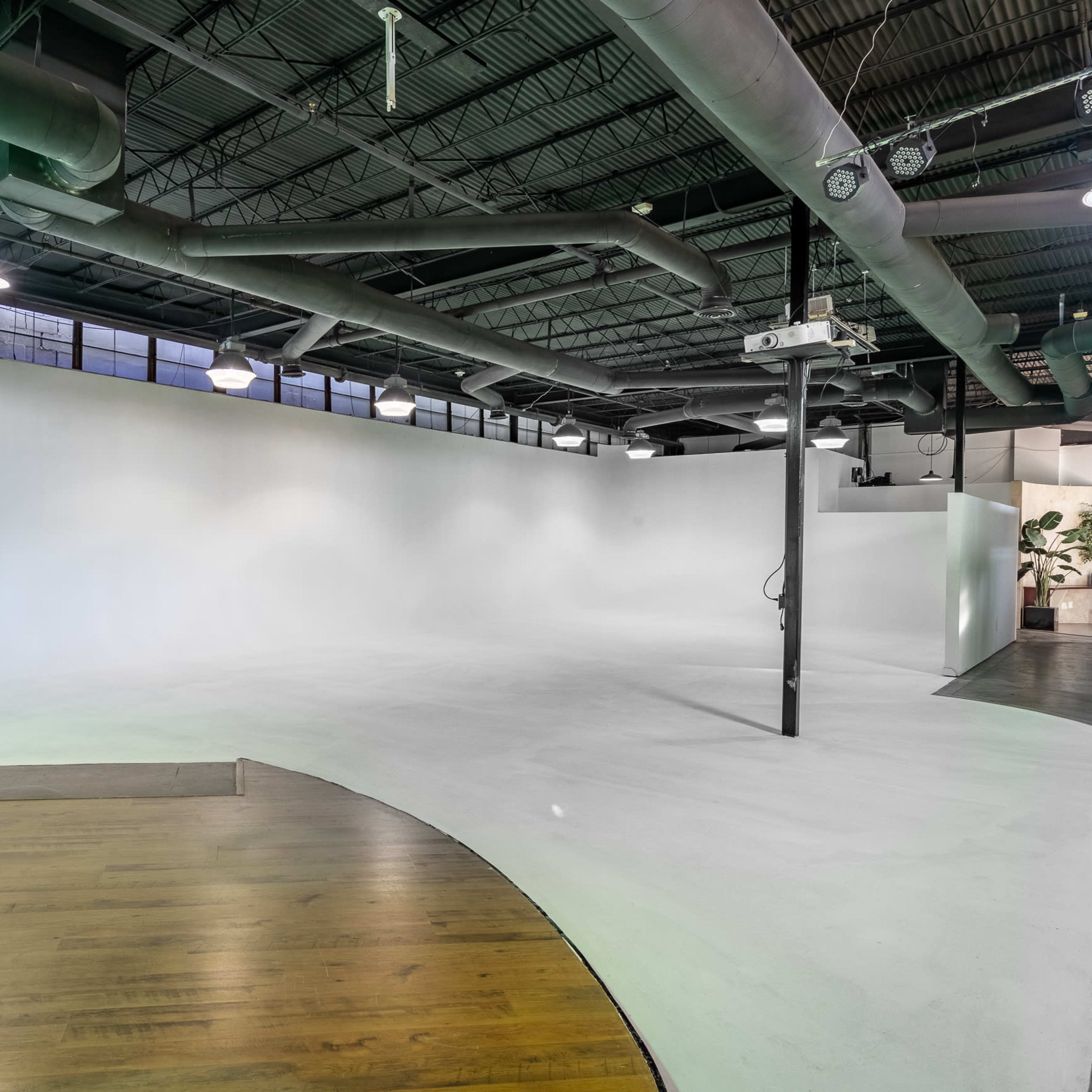 A spacious interior with a curved wooden floor, a large white wall, and industrial-style ceiling features.