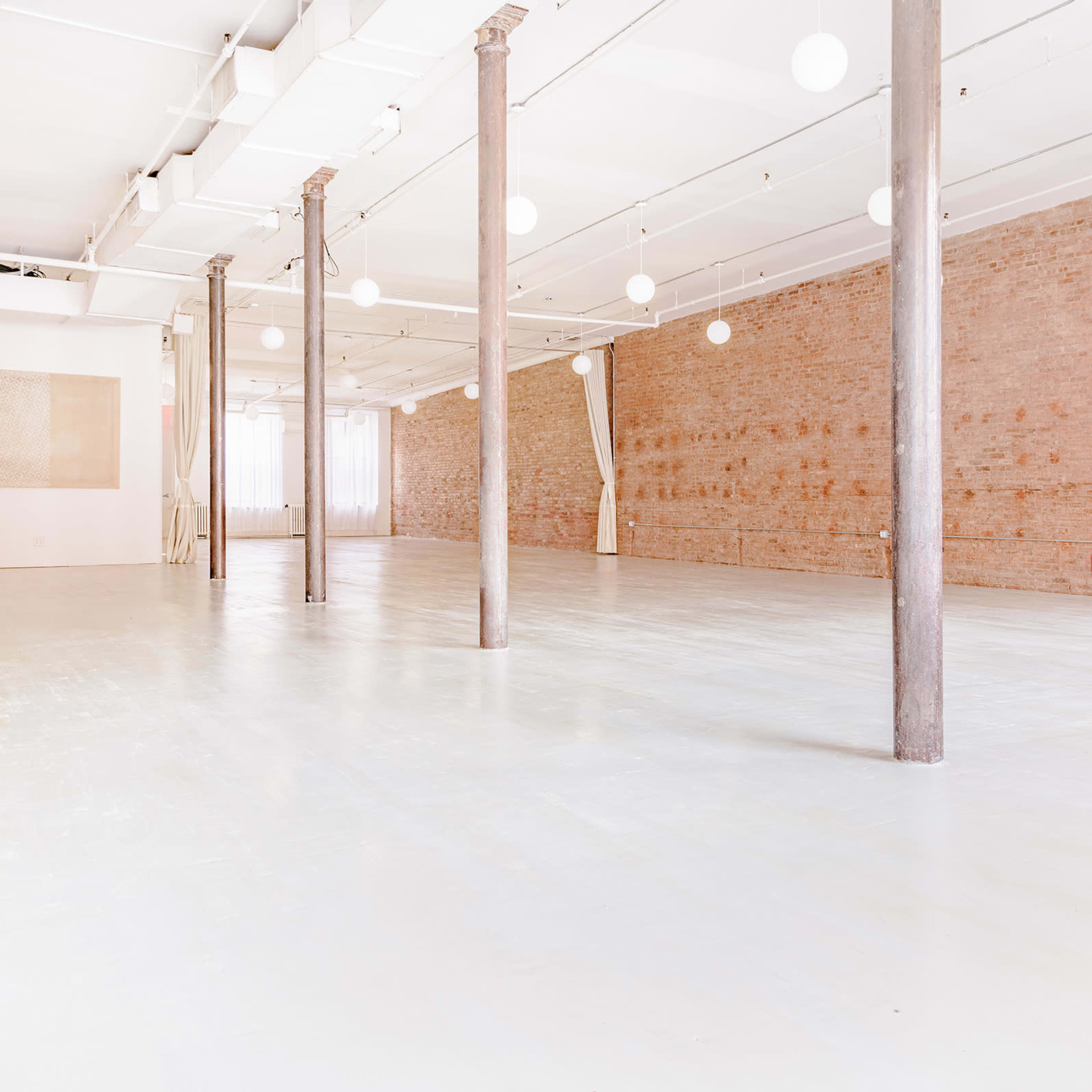 A spacious, empty room with wooden pillars, a light-colored floor, and exposed brick walls.