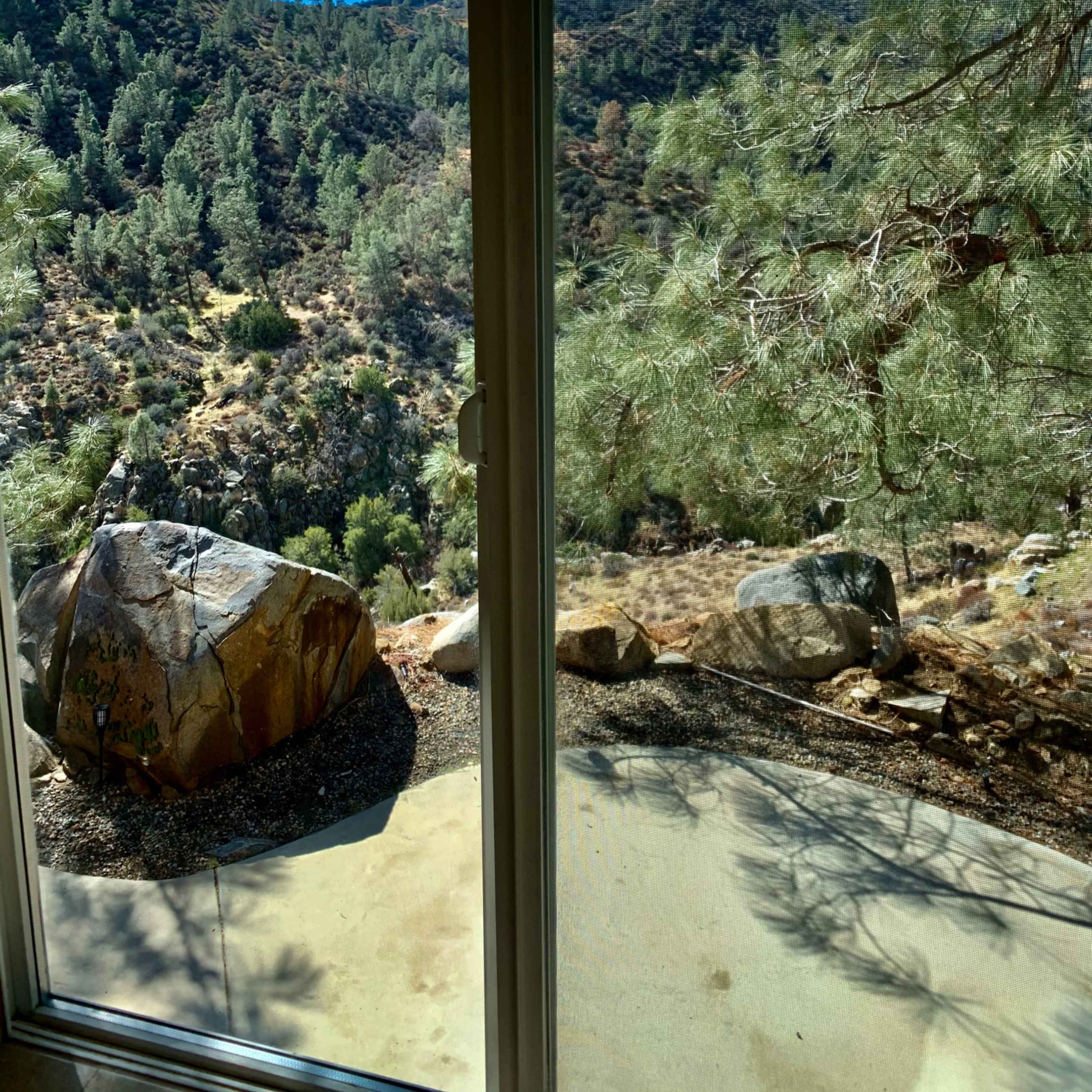 The view through the glass sliding door shows a mountainous landscape with trees and large boulders.