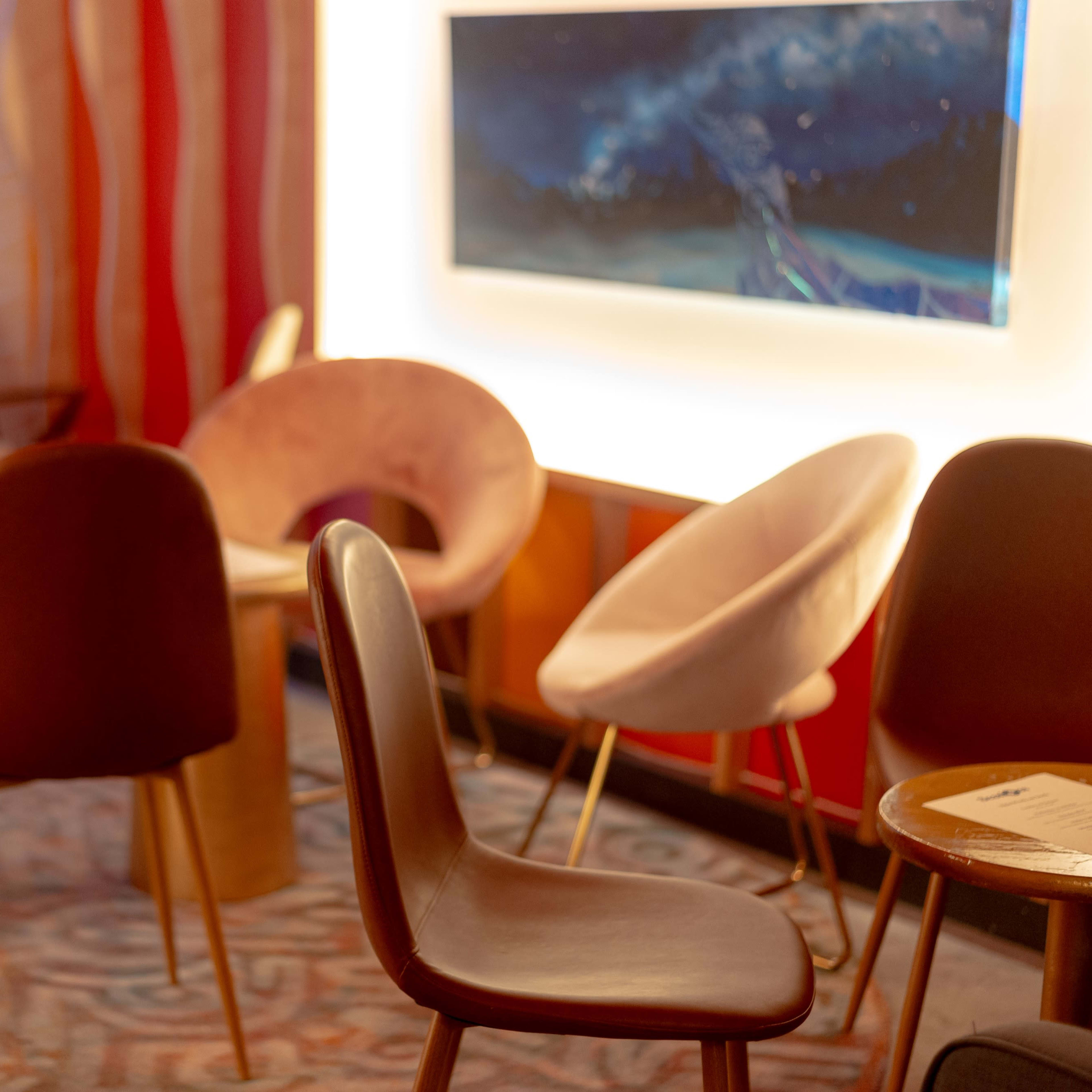 A cozy lounge area features several modern chairs and tables, with a wall-mounted artwork in the background.