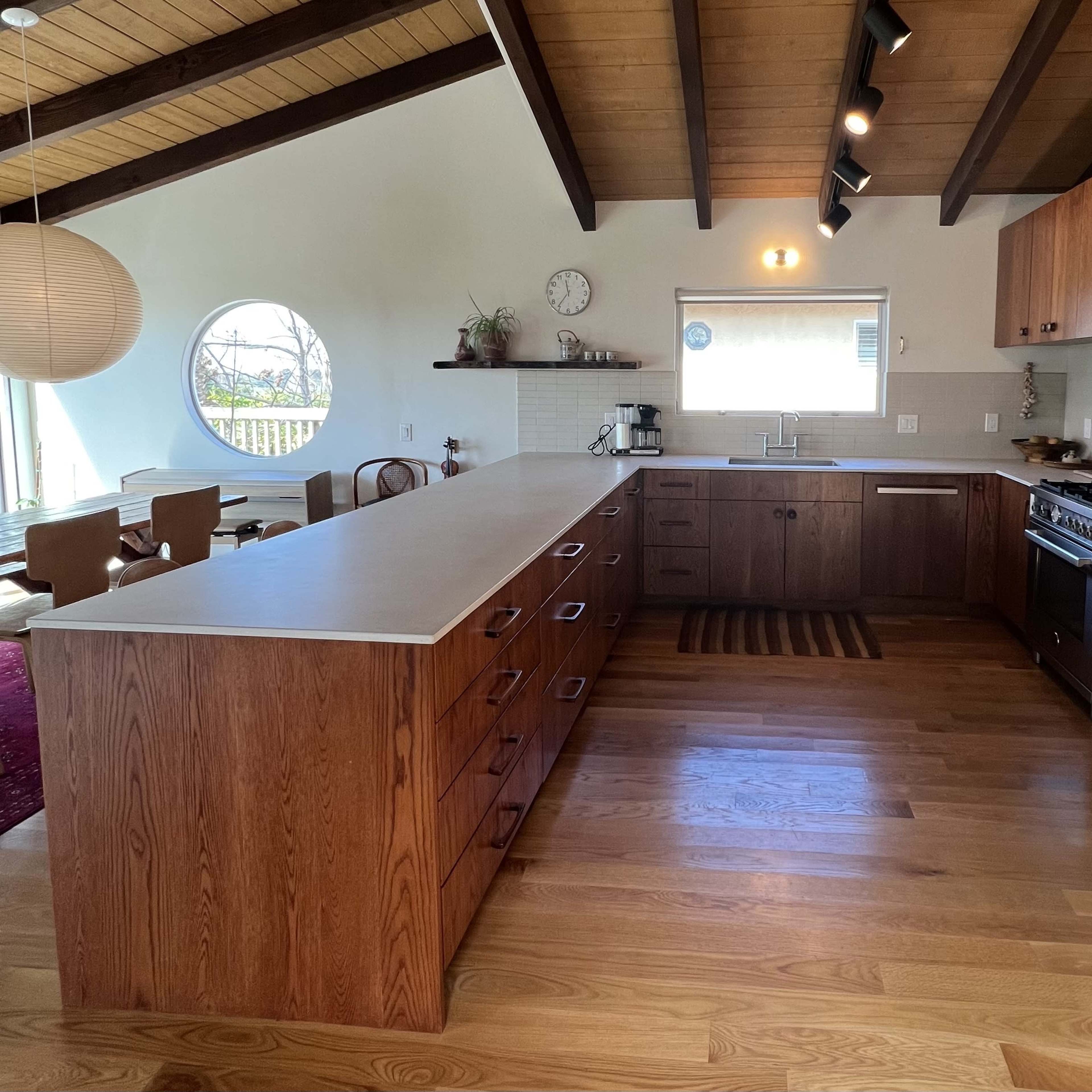 The kitchen features wooden cabinets, a large island with a countertop, and a round window, creating an open and modern space.