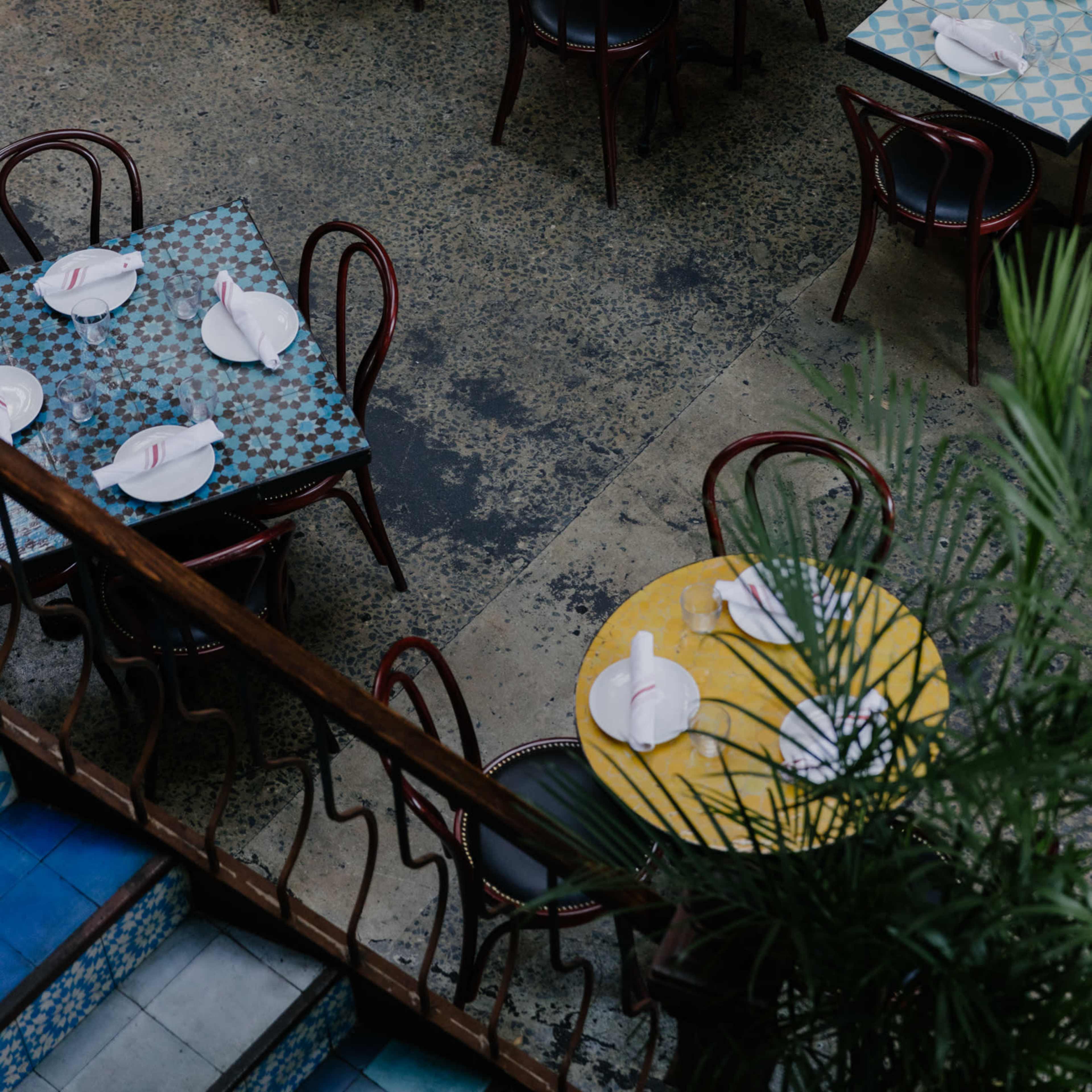 An aerial view of a restaurant interior with tables featuring colorful patterned tablecloths and neatly arranged plates.