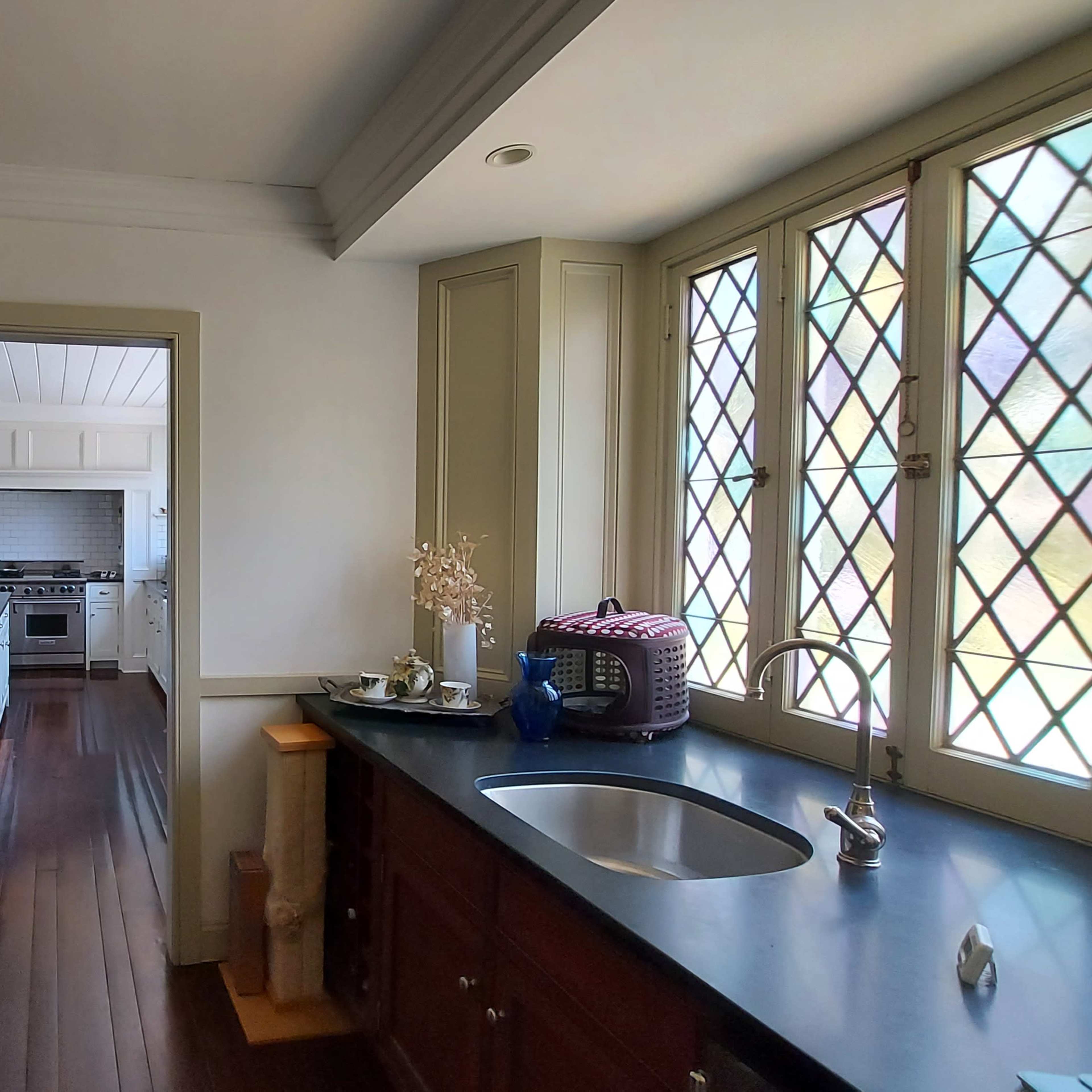 A kitchen with wooden cabinets and a view of a dining area through a doorway, featuring a sink and stained glass windows.