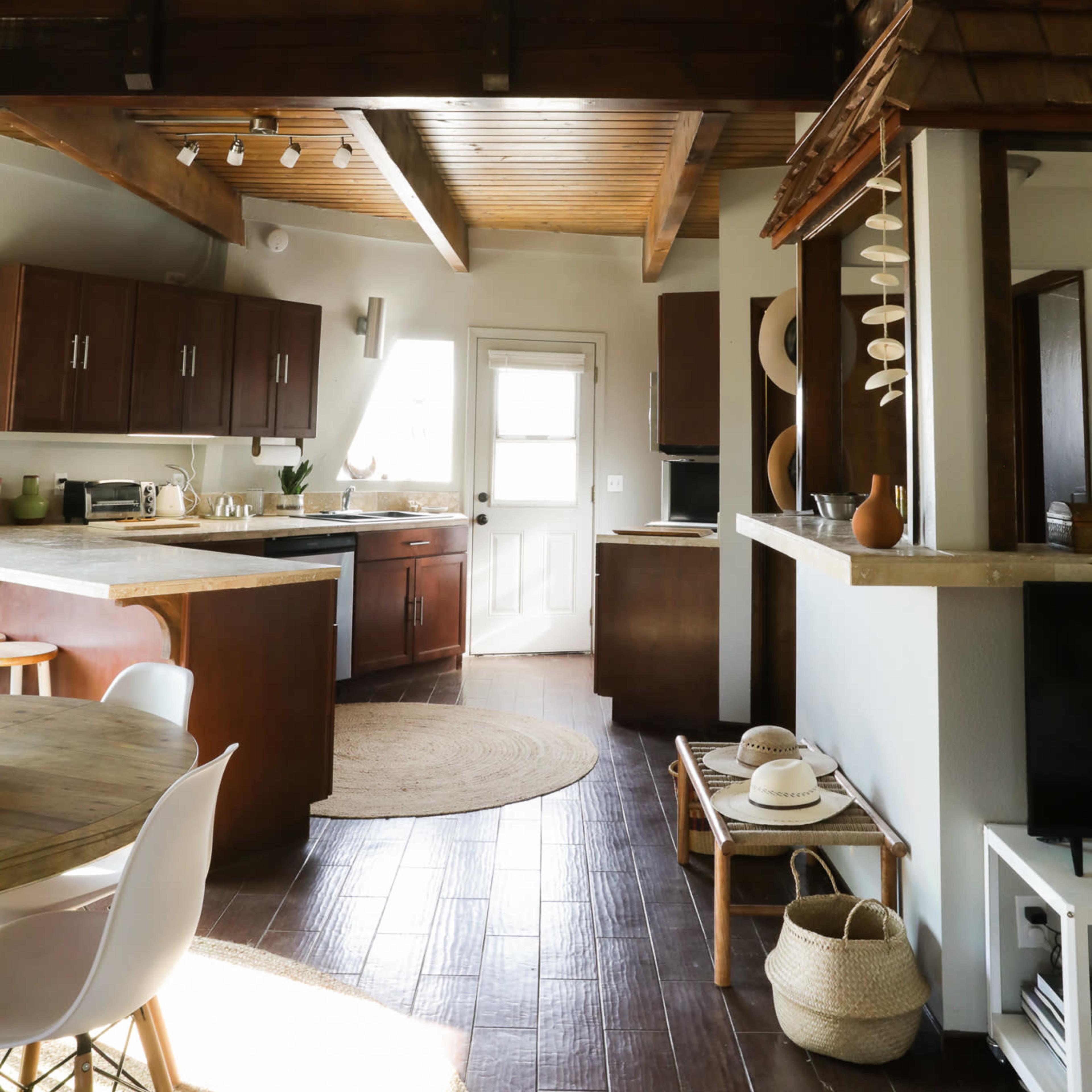A modern kitchen and dining area with a lofted ceiling, featuring wooden cabinetry and a circular rug.