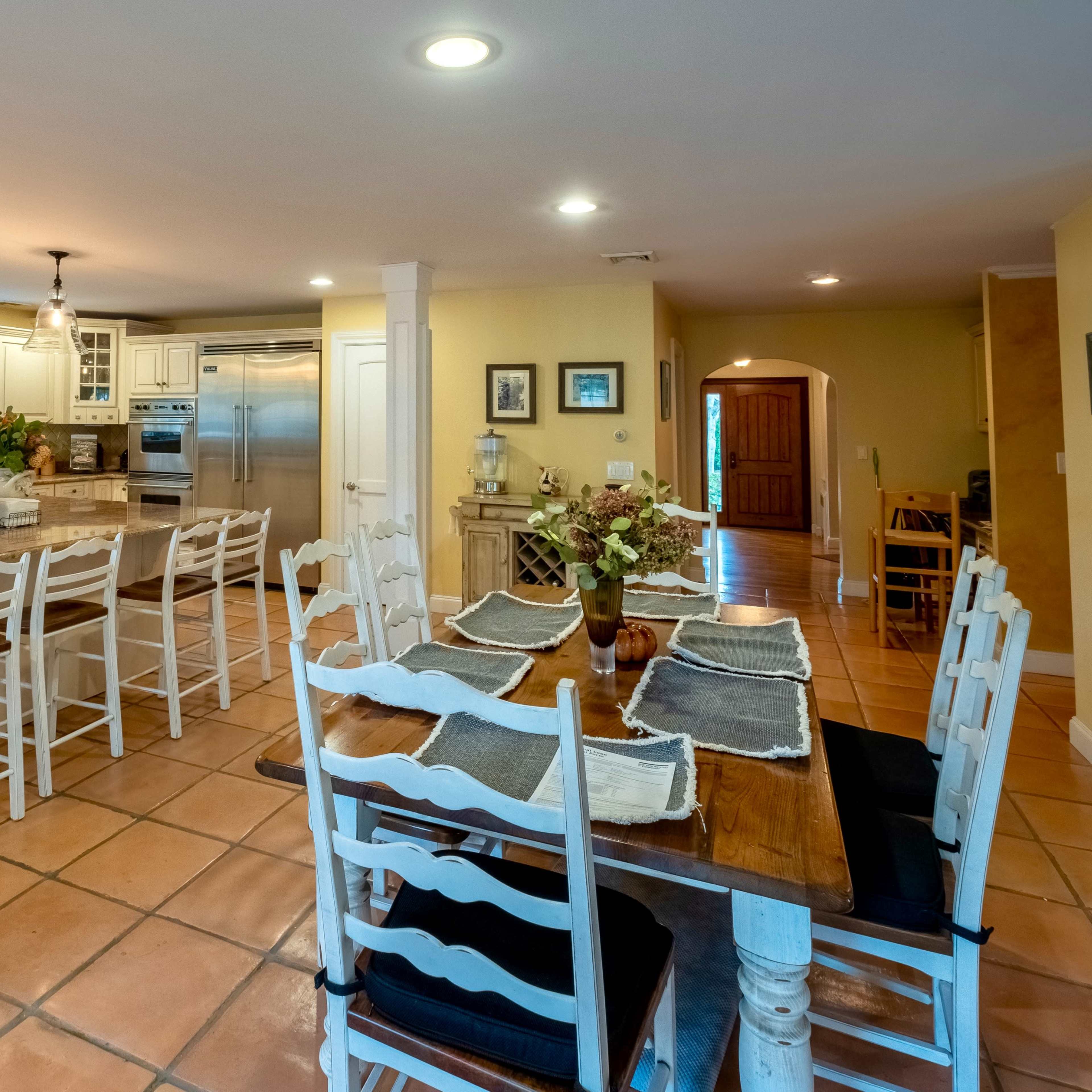 A spacious kitchen featuring a central island with bar seating, a wooden dining table, and tile flooring.