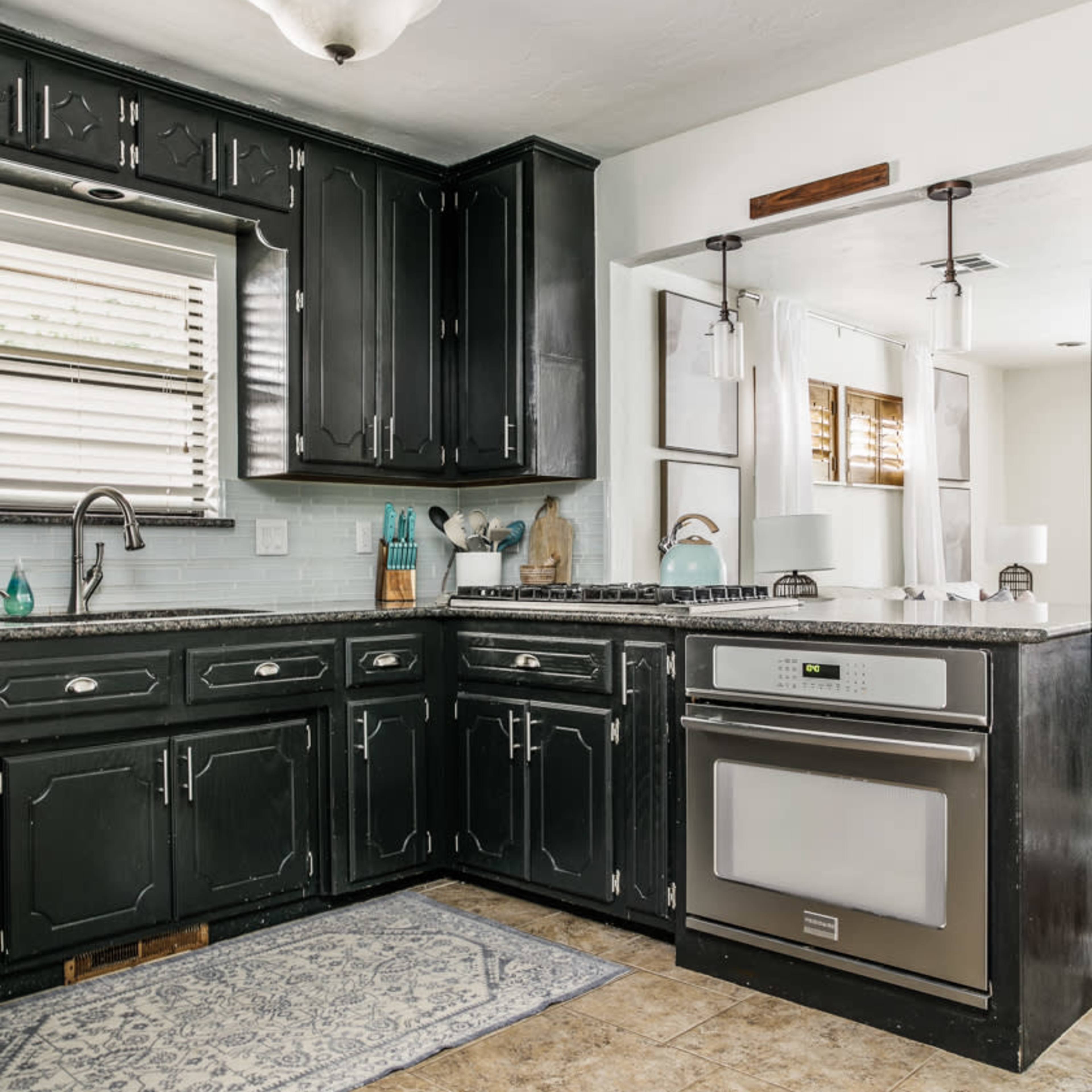 A kitchen with black cabinetry, a stainless steel oven, and a light-colored stone countertop.