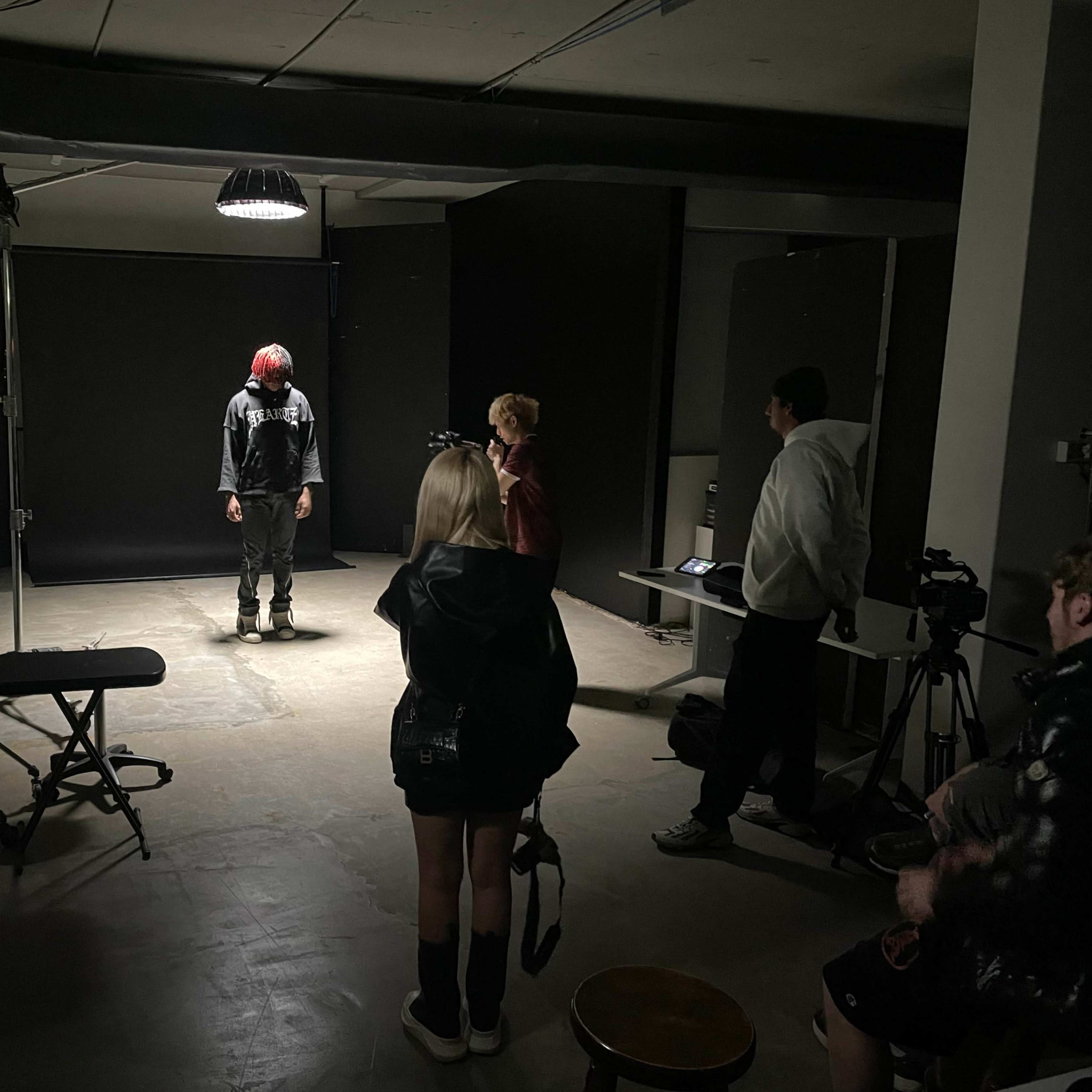 A group of individuals observes a person standing under a spotlight in a photography studio.