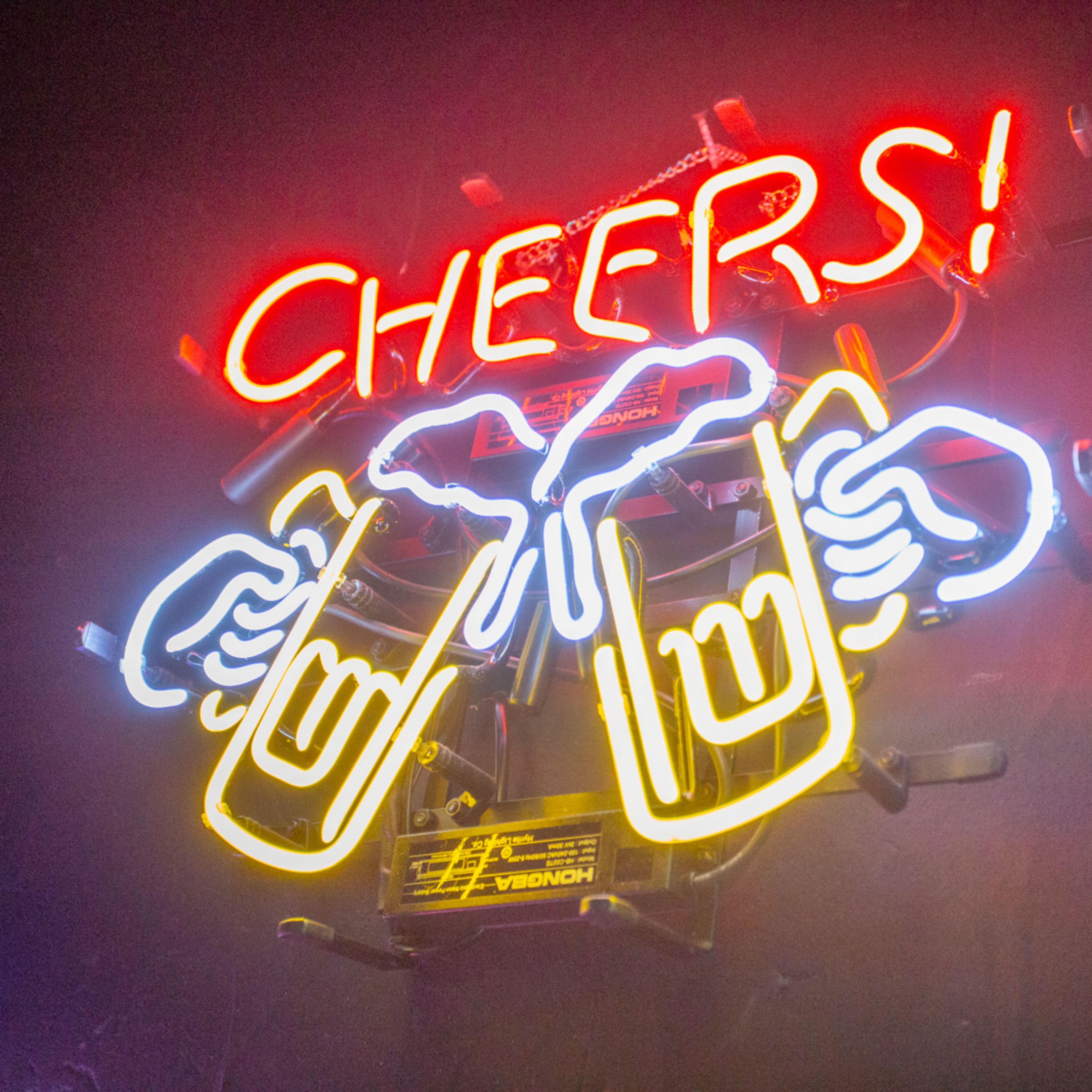 A neon sign displays the word "CHEERS!" along with graphic images of two mugs clinking together.