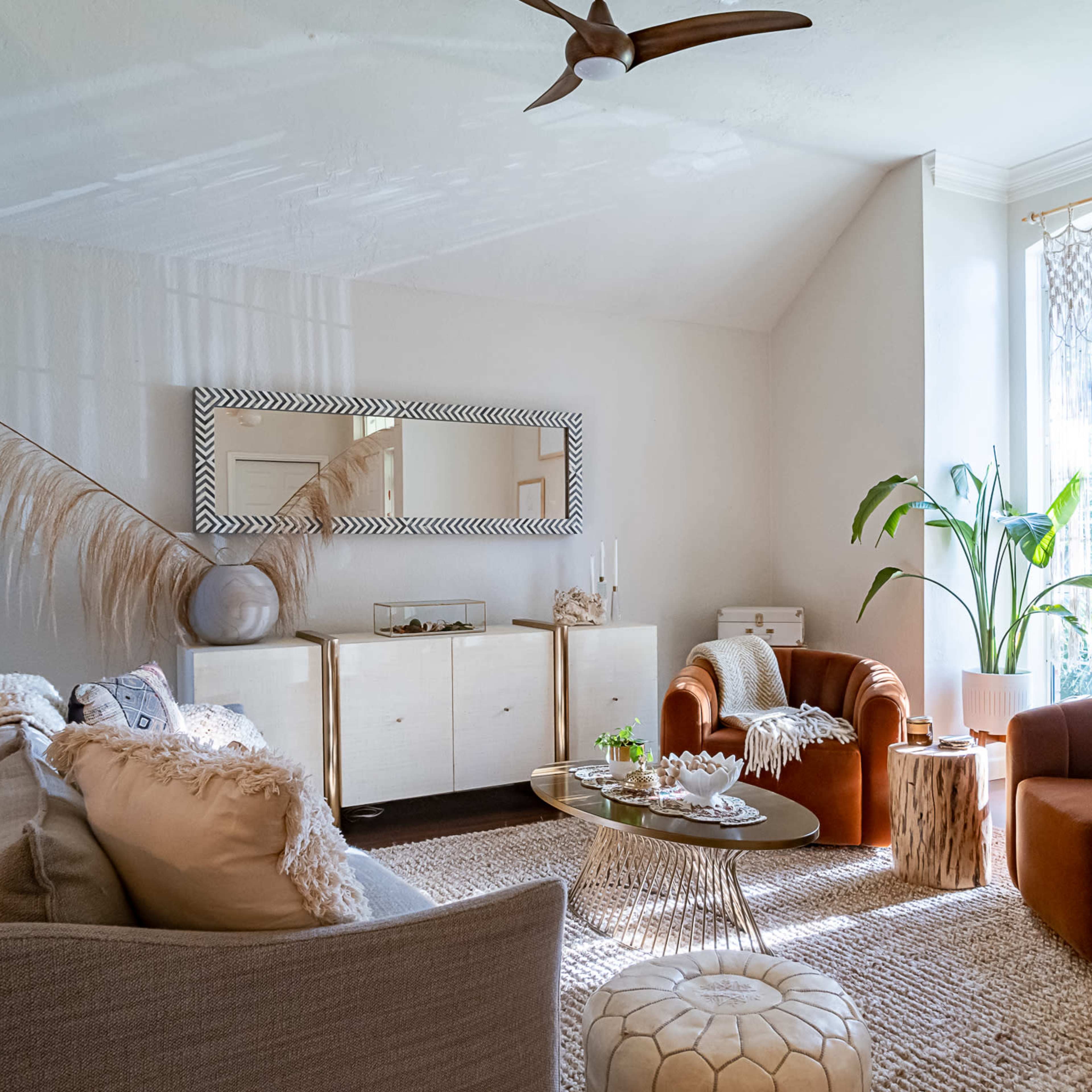 The living room features two armchairs, a beige sofa, a decorative mirror, a light rug, and a potted plant near a window.