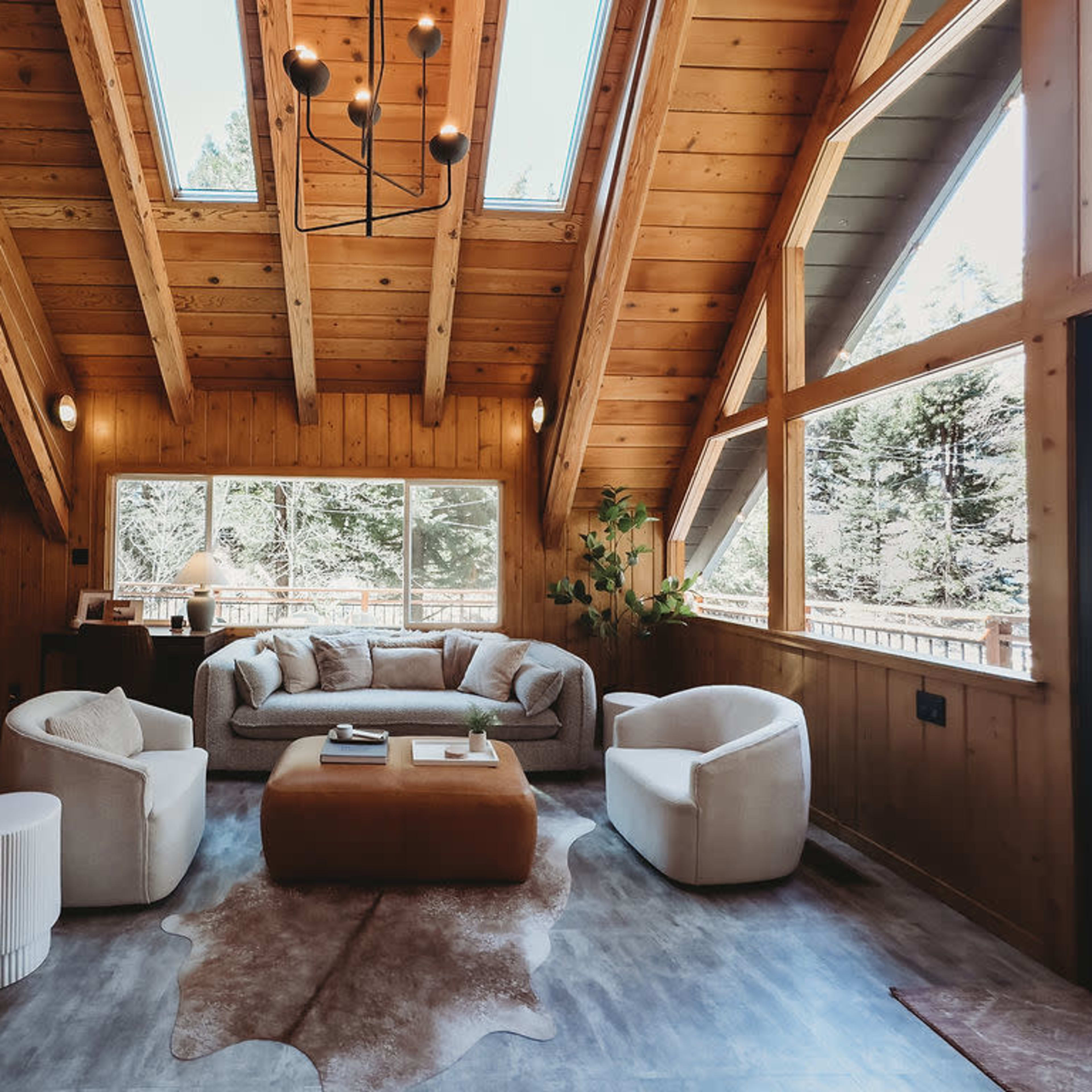 A cozy living room with wooden walls, a vaulted ceiling, large windows, and modern furnishings.