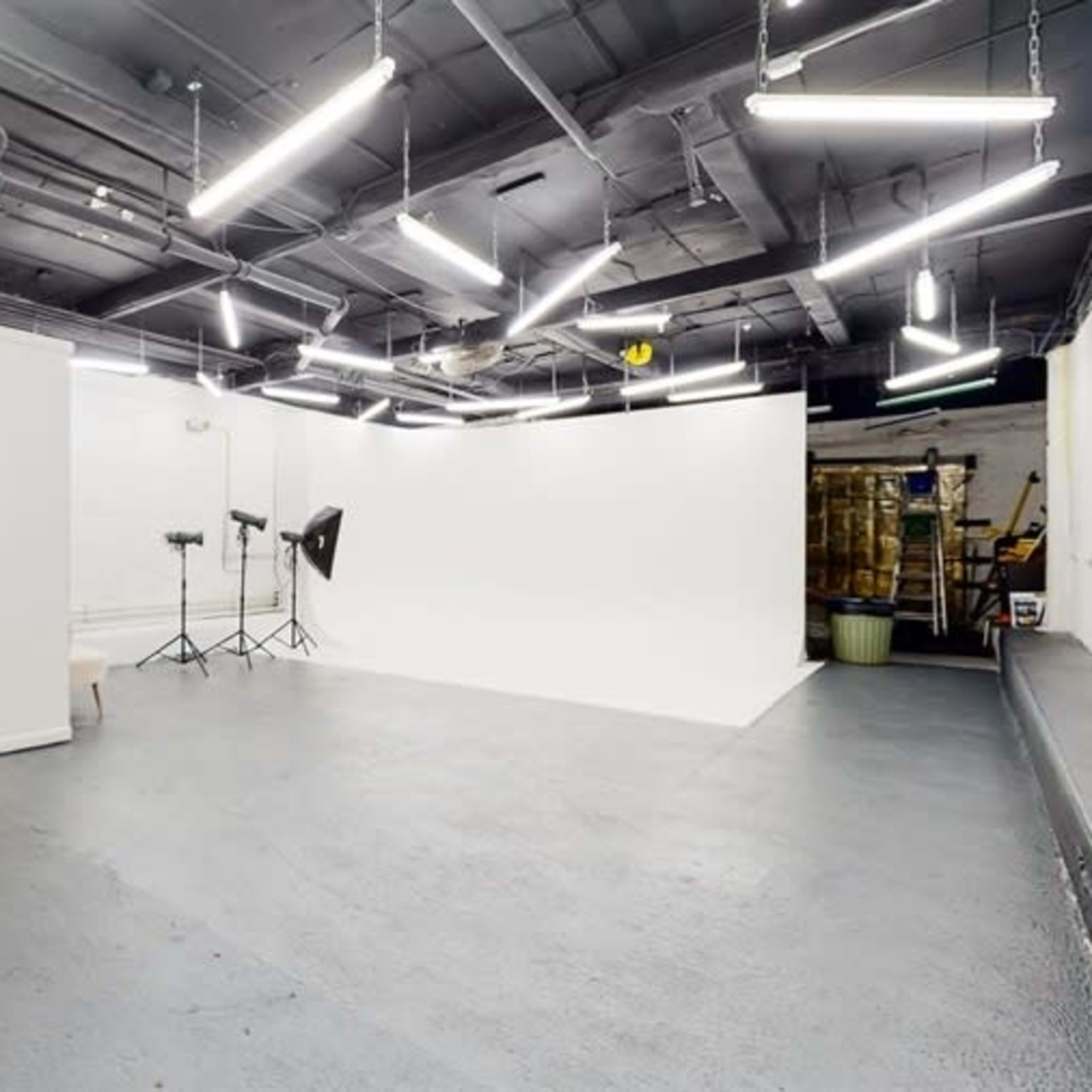 A photography studio with a white backdrop, two lights on stands, and a restroom area in the corner.