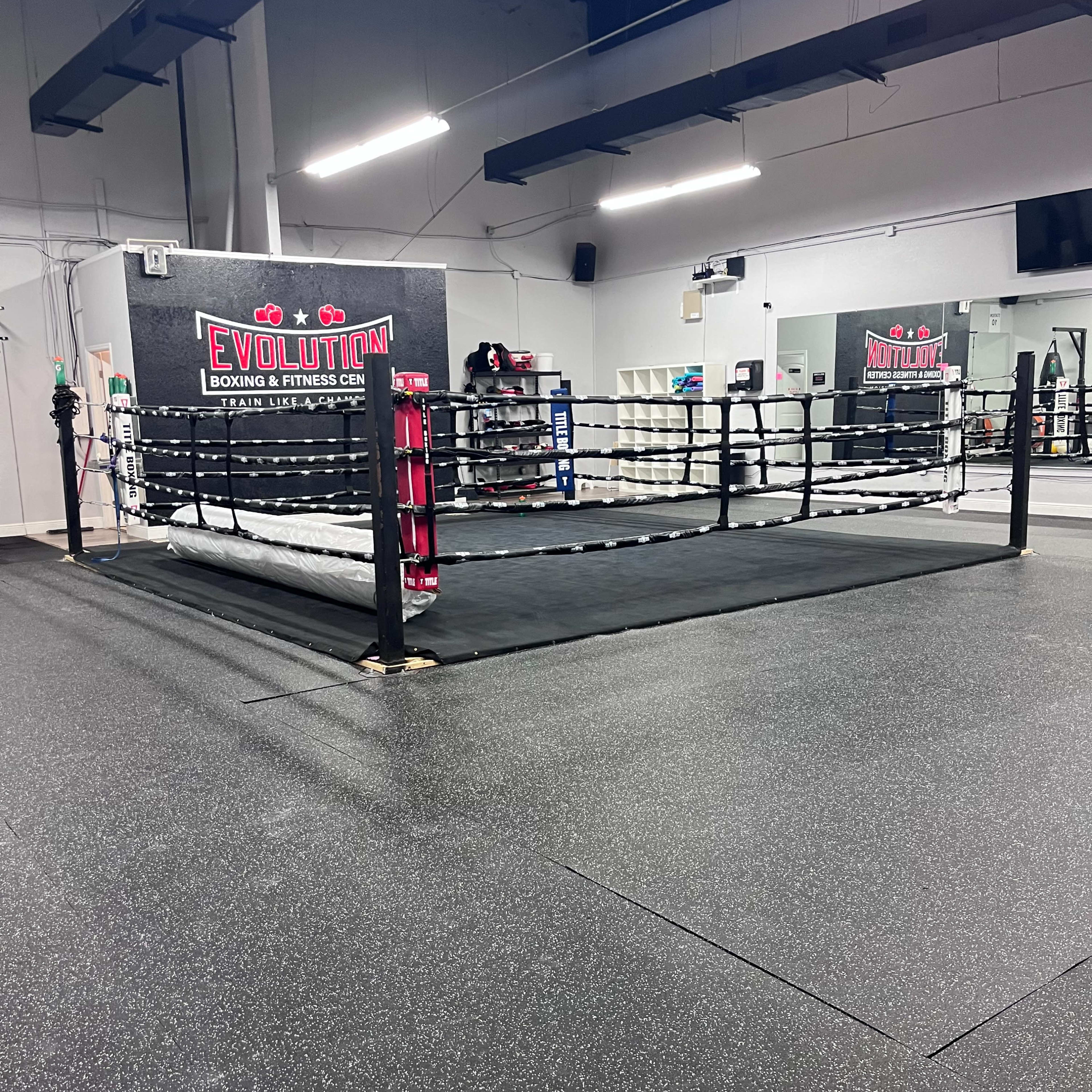 A boxing ring in a gym with a rubberized floor and a wall featuring the word "EVOLUTION."