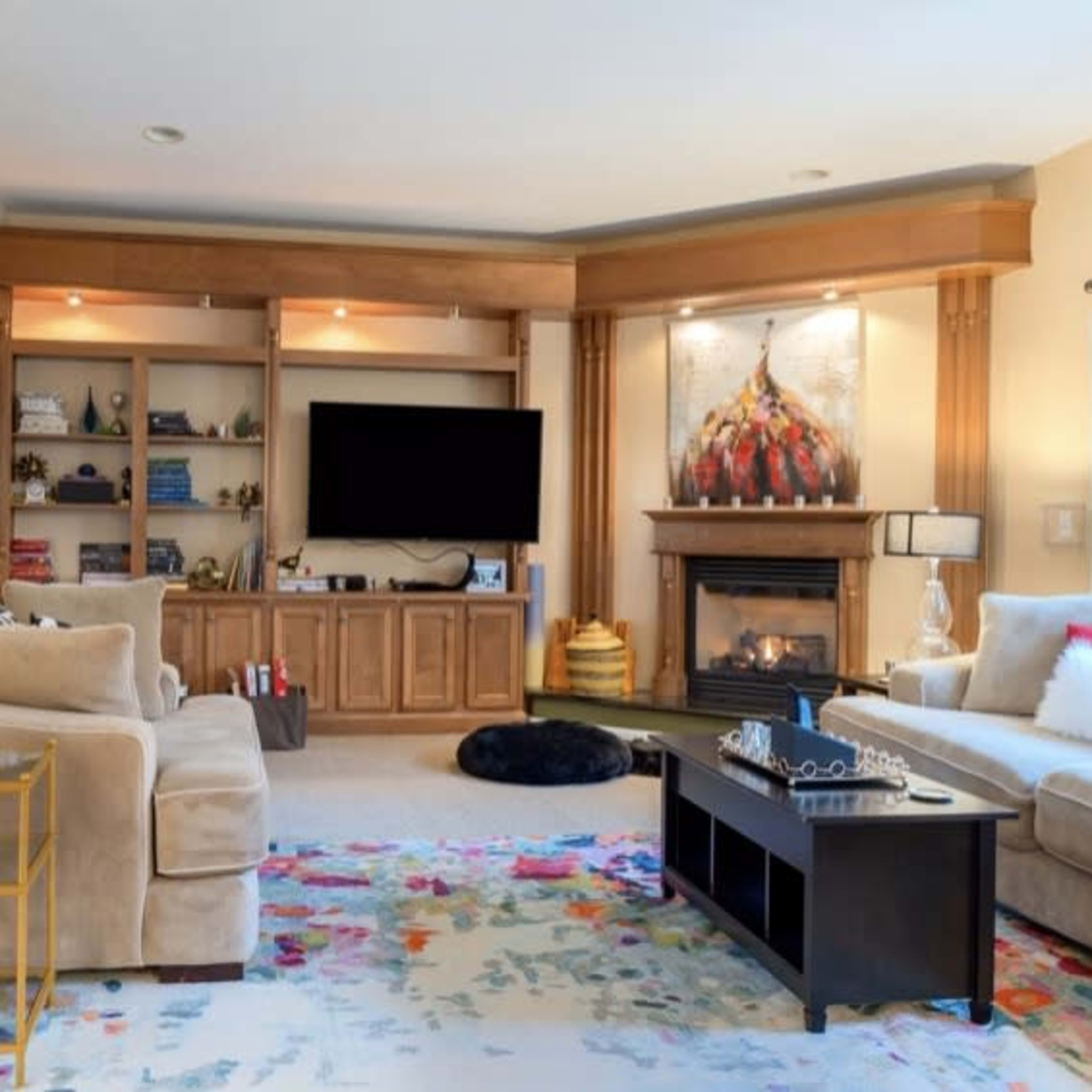 A cozy living room features a fireplace, a large television, and a mix of comfortable seating arranged around a colorful area rug.