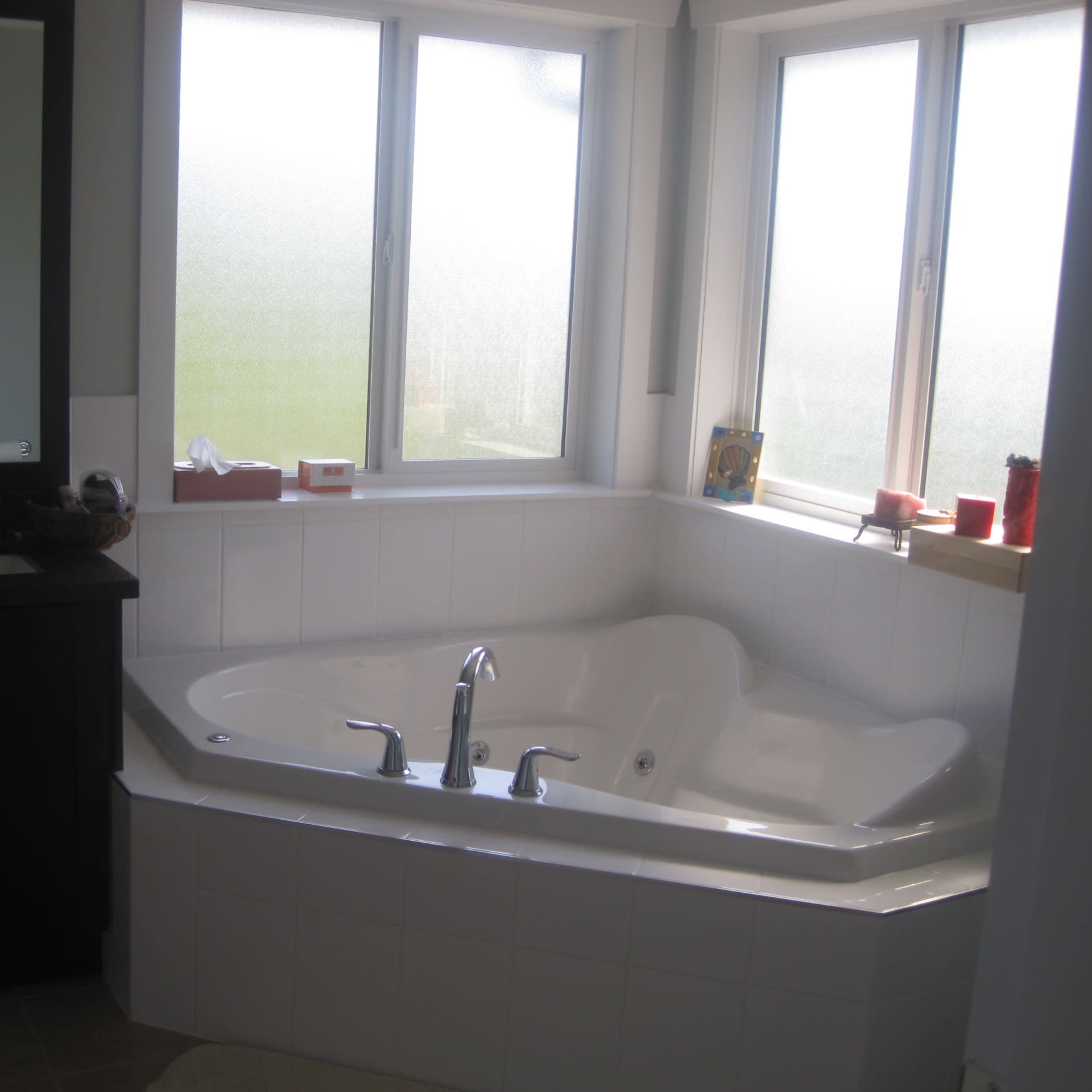 A bathroom featuring a corner jetted bathtub, a dark vanity with a mirror, and large windows allowing natural light.
