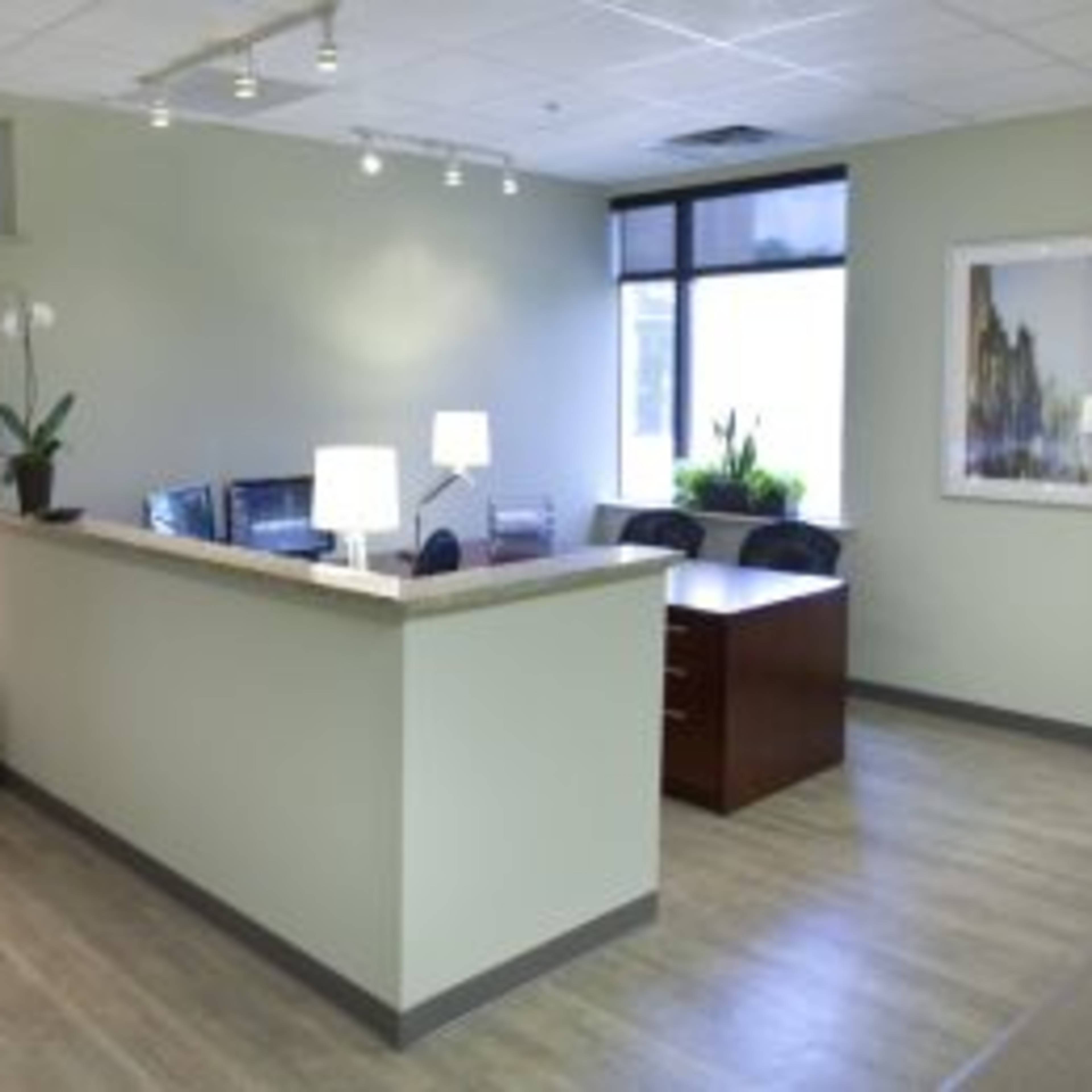 A modern office reception area with seating, a desk, and artwork on the walls.