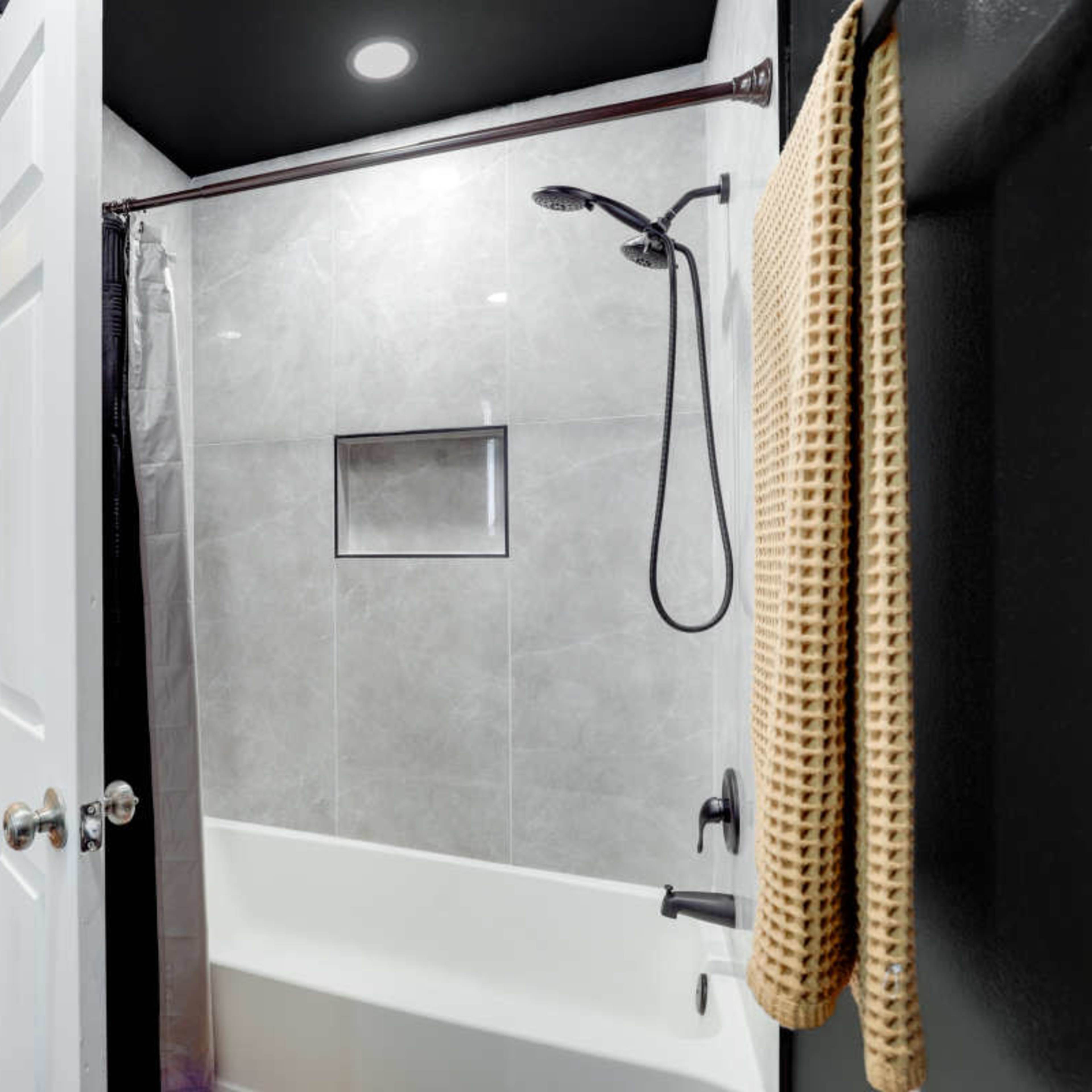 A modern bathroom with a glass-enclosed shower, a bathtub, and a towel hanging near the entrance.