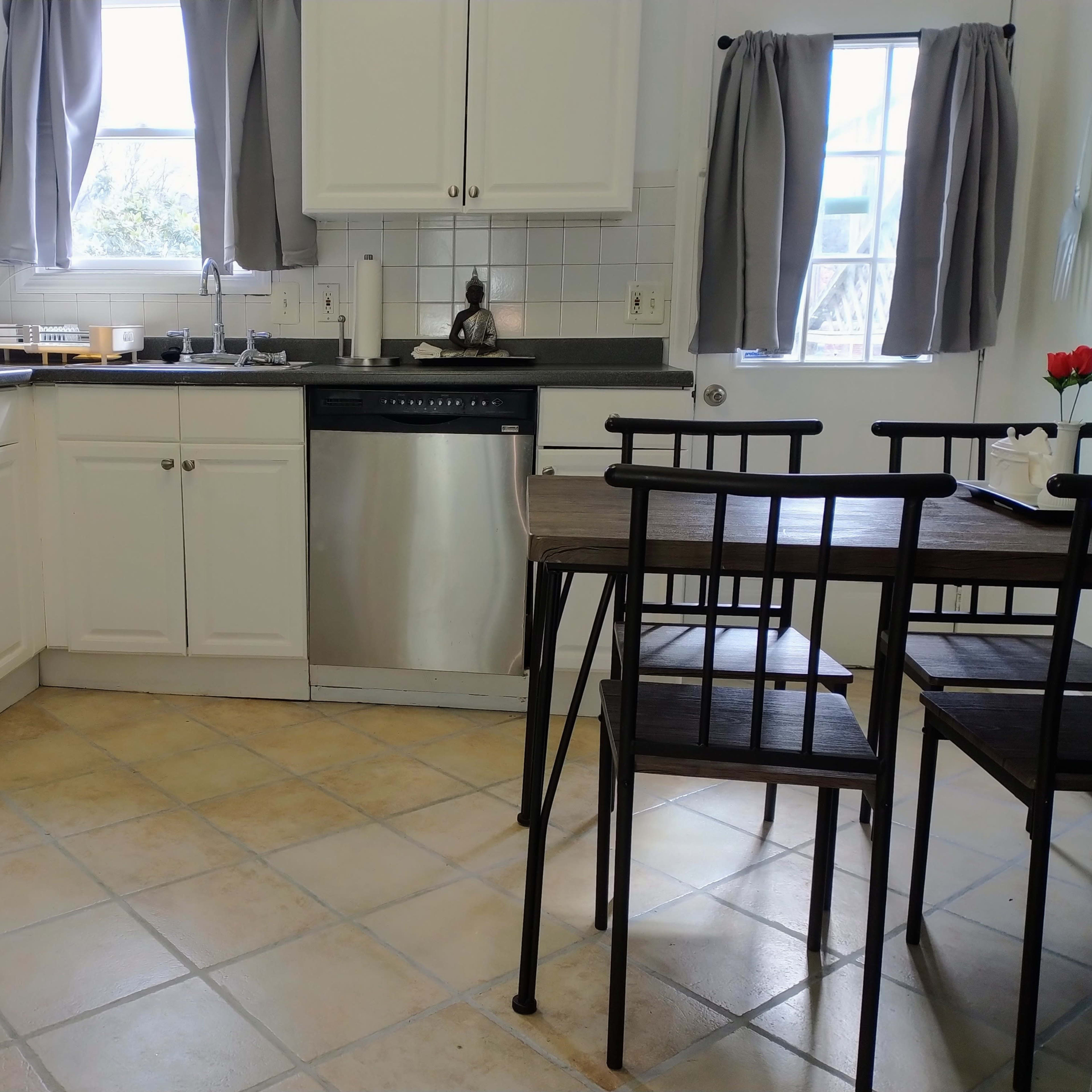 A kitchen with a stainless steel oven and dishwasher, white cabinets, and a small wooden dining table with metal chairs.