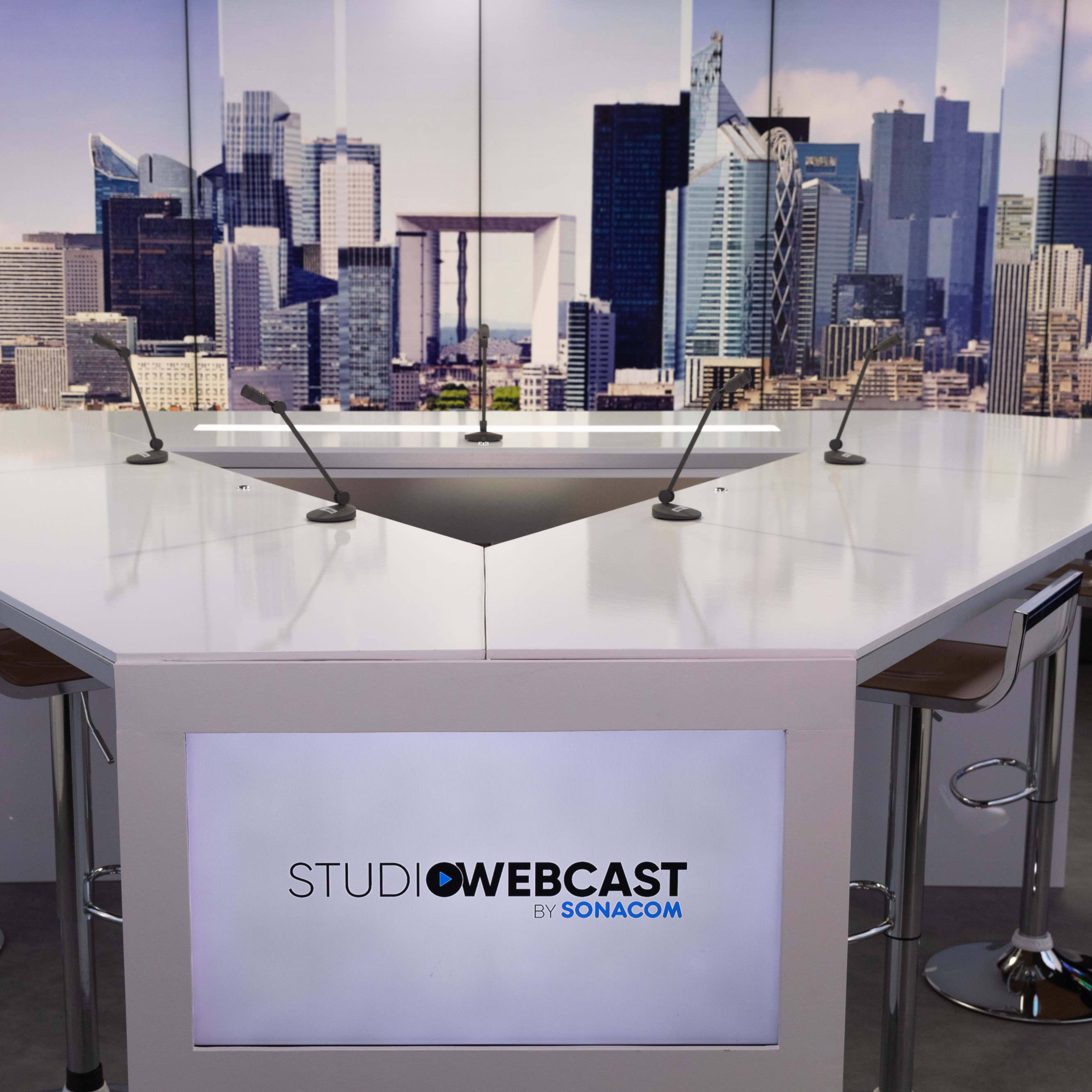 A modern studio setup with a white table and several chairs, featuring a large city skyline backdrop.