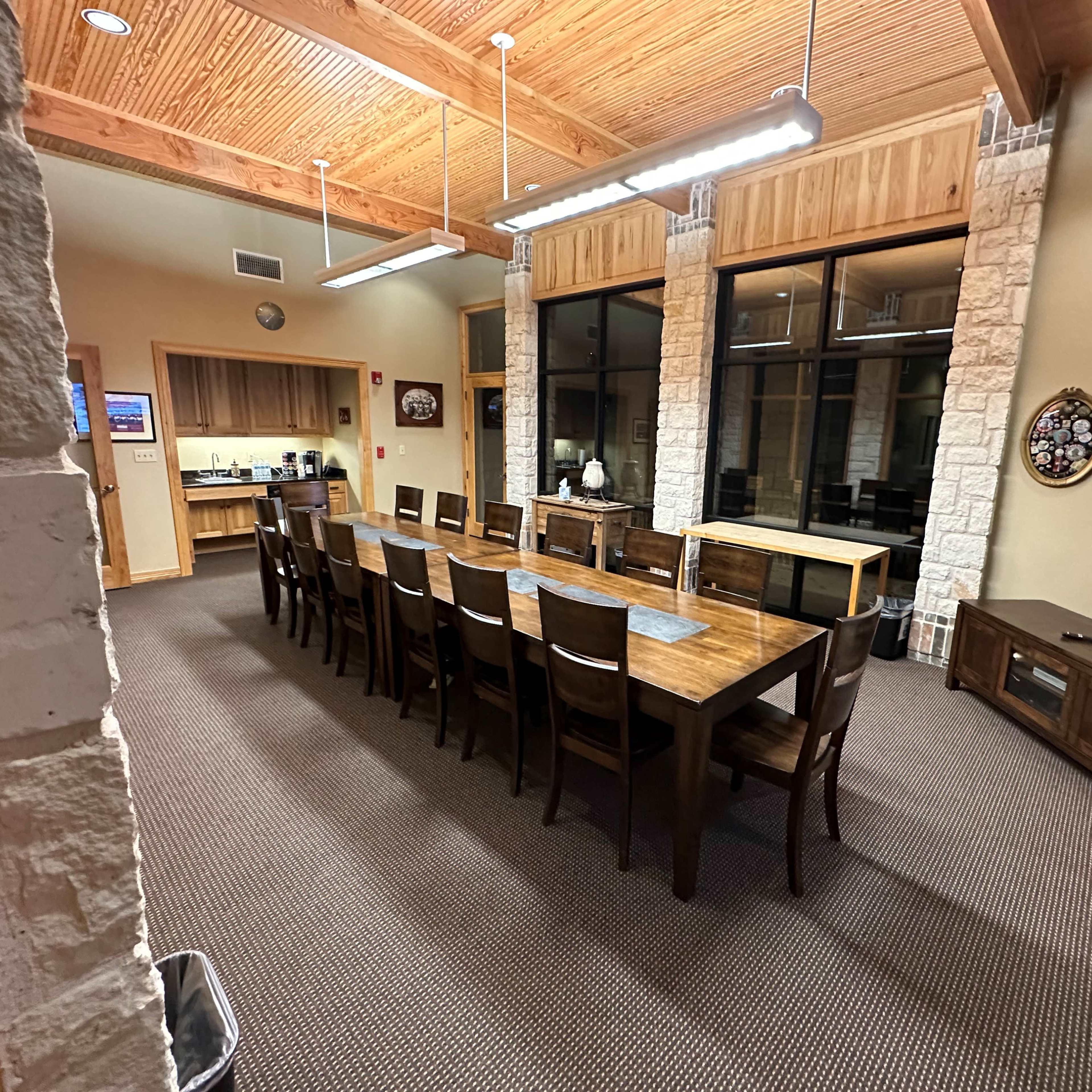A large, wood-framed conference room with a long wooden table and multiple chairs, surrounded by windows and stone accents.