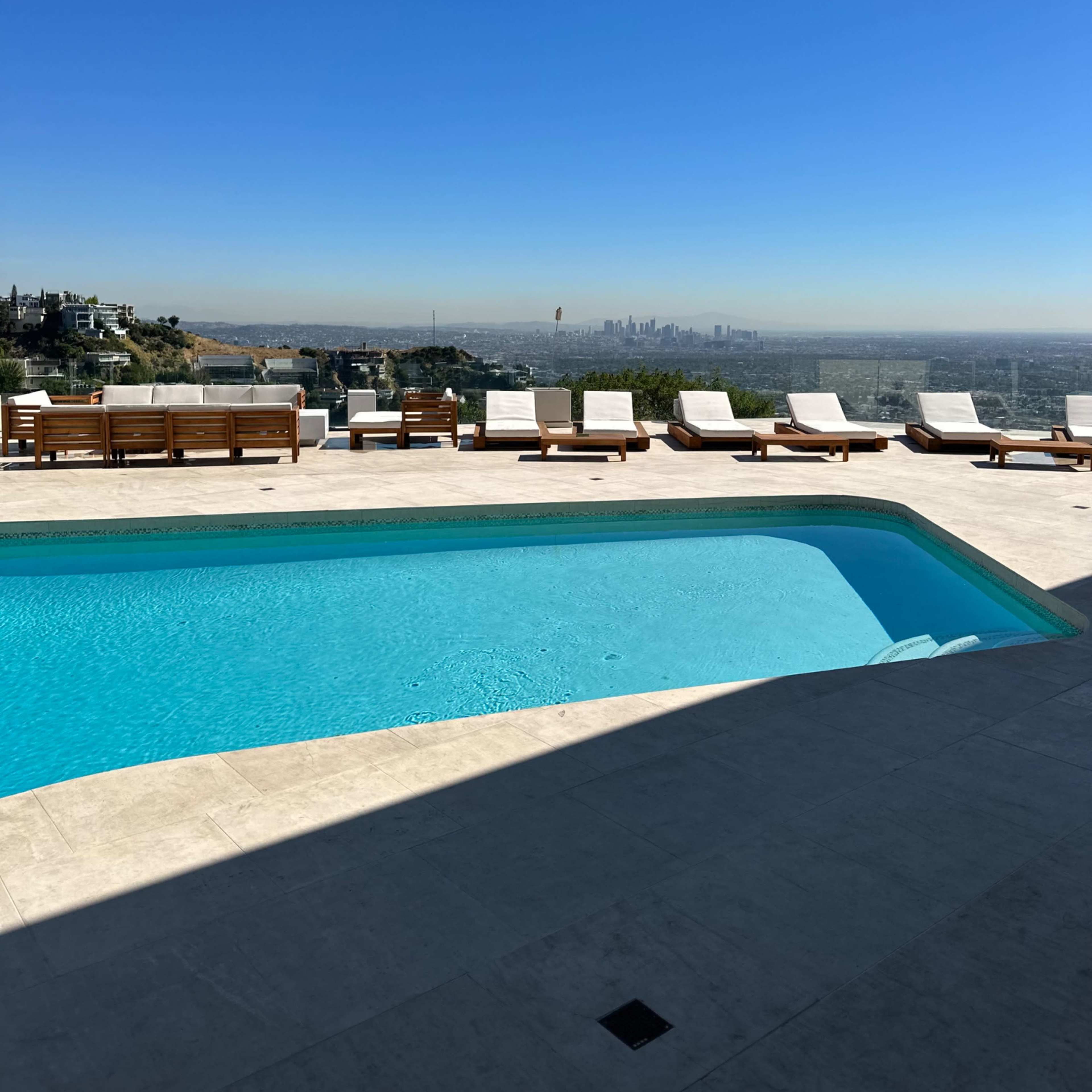 A swimming pool with lounge chairs surrounds it overlooks a city skyline under a clear blue sky.