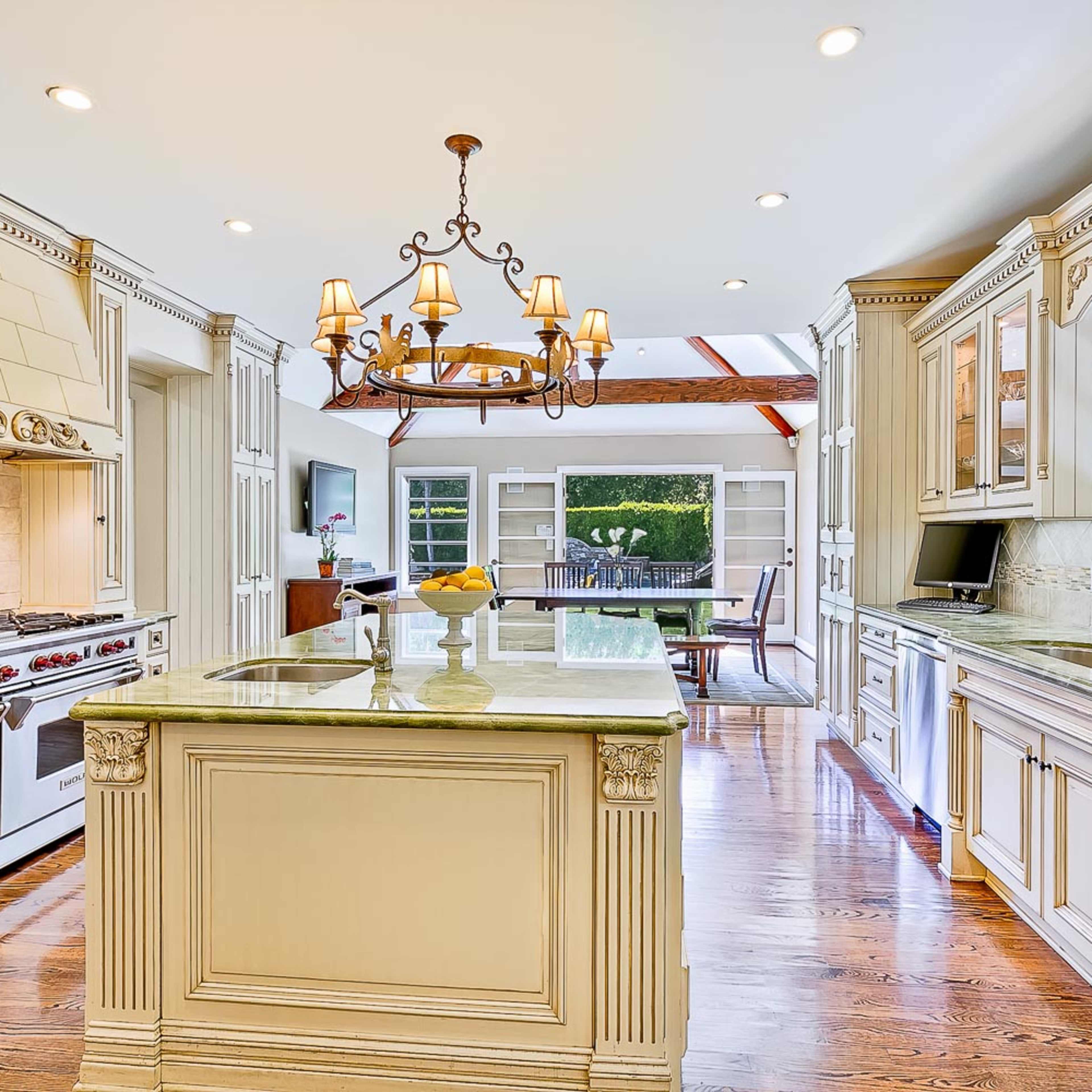 A bright and spacious kitchen featuring a central island, a chandelier, and large windows overlooking an outdoor patio.