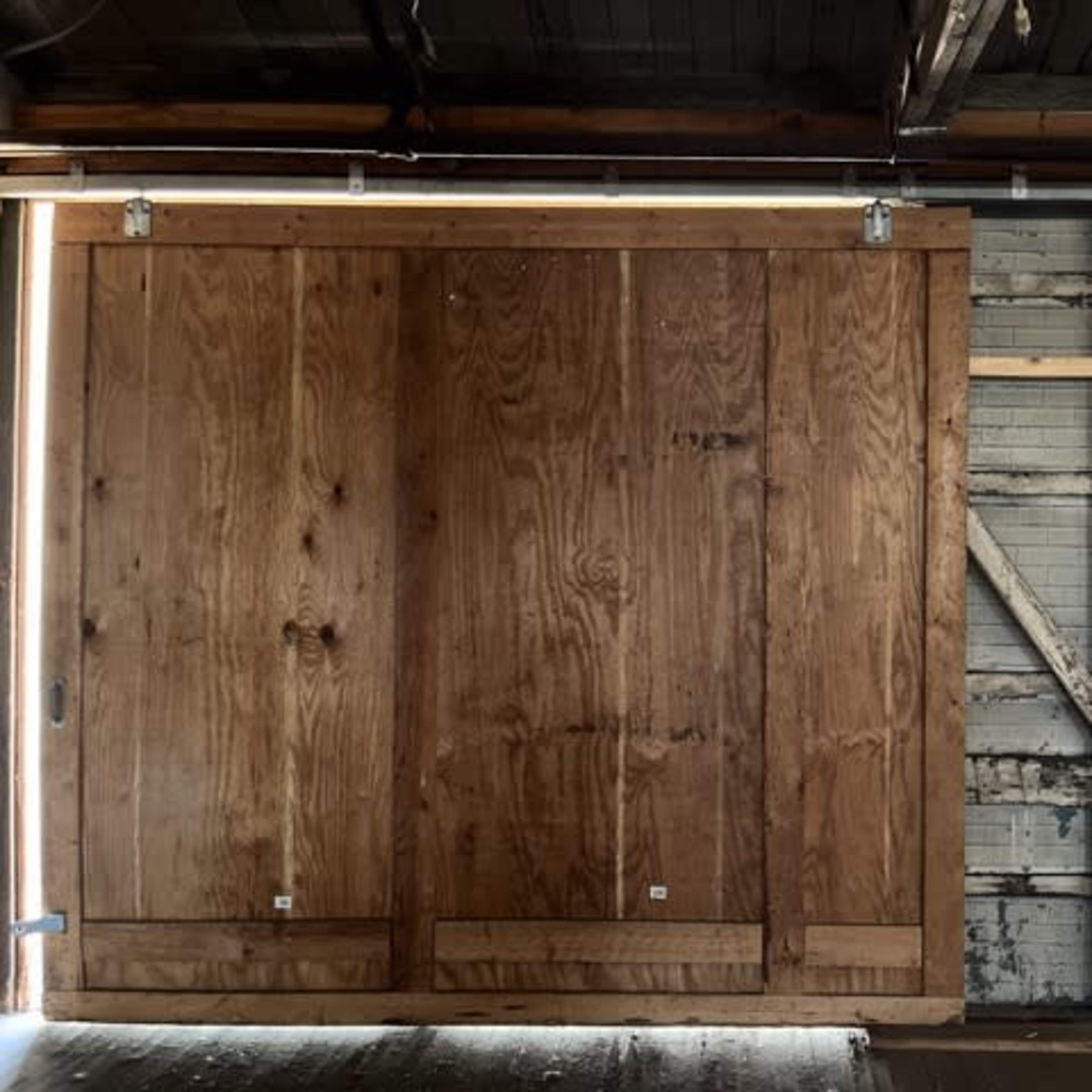 A large wooden sliding door mounted on a metal track, set against a weathered wall with exposed sections and beams.