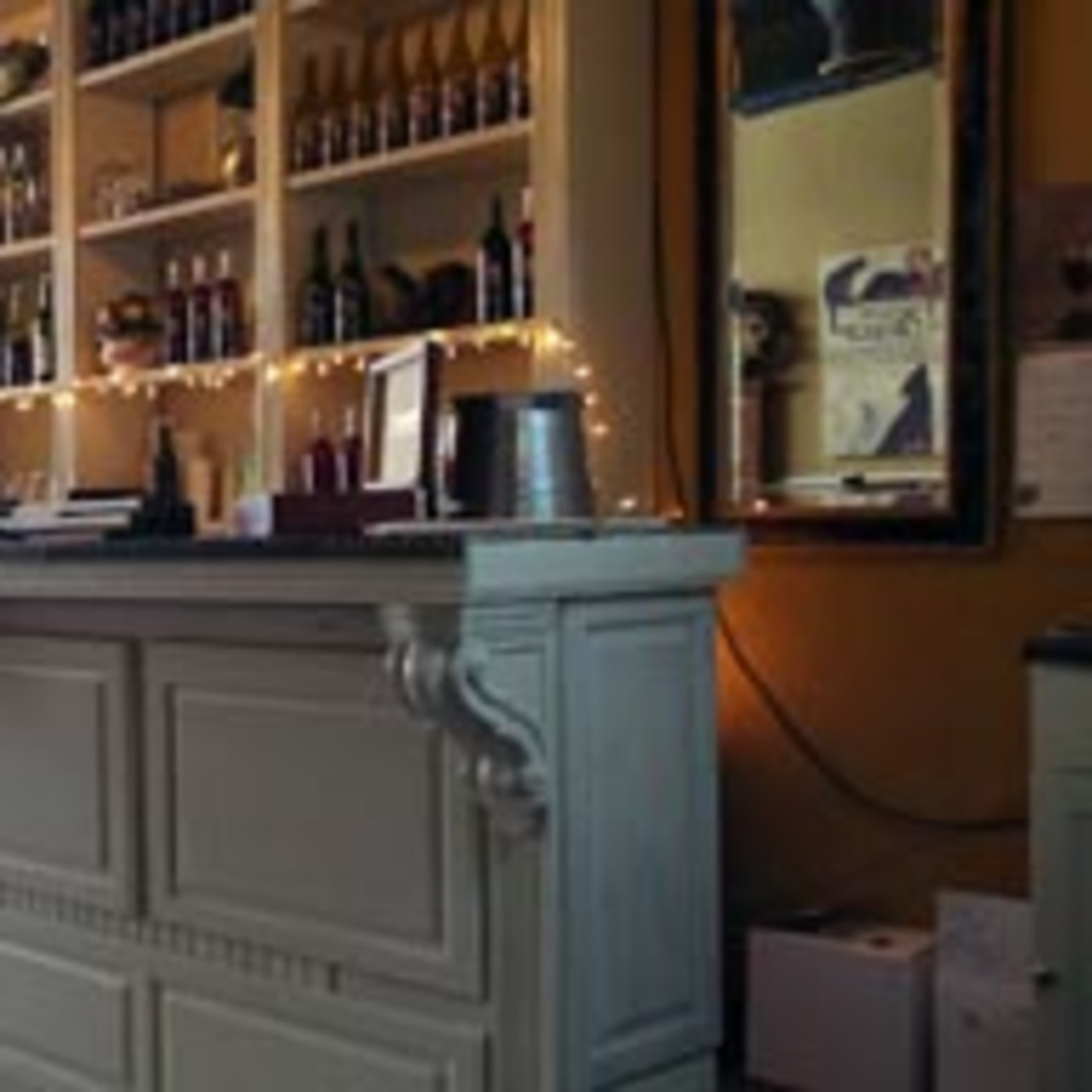 A wooden bar with a neatly organized shelf of bottles and a mirror on the wall behind it.