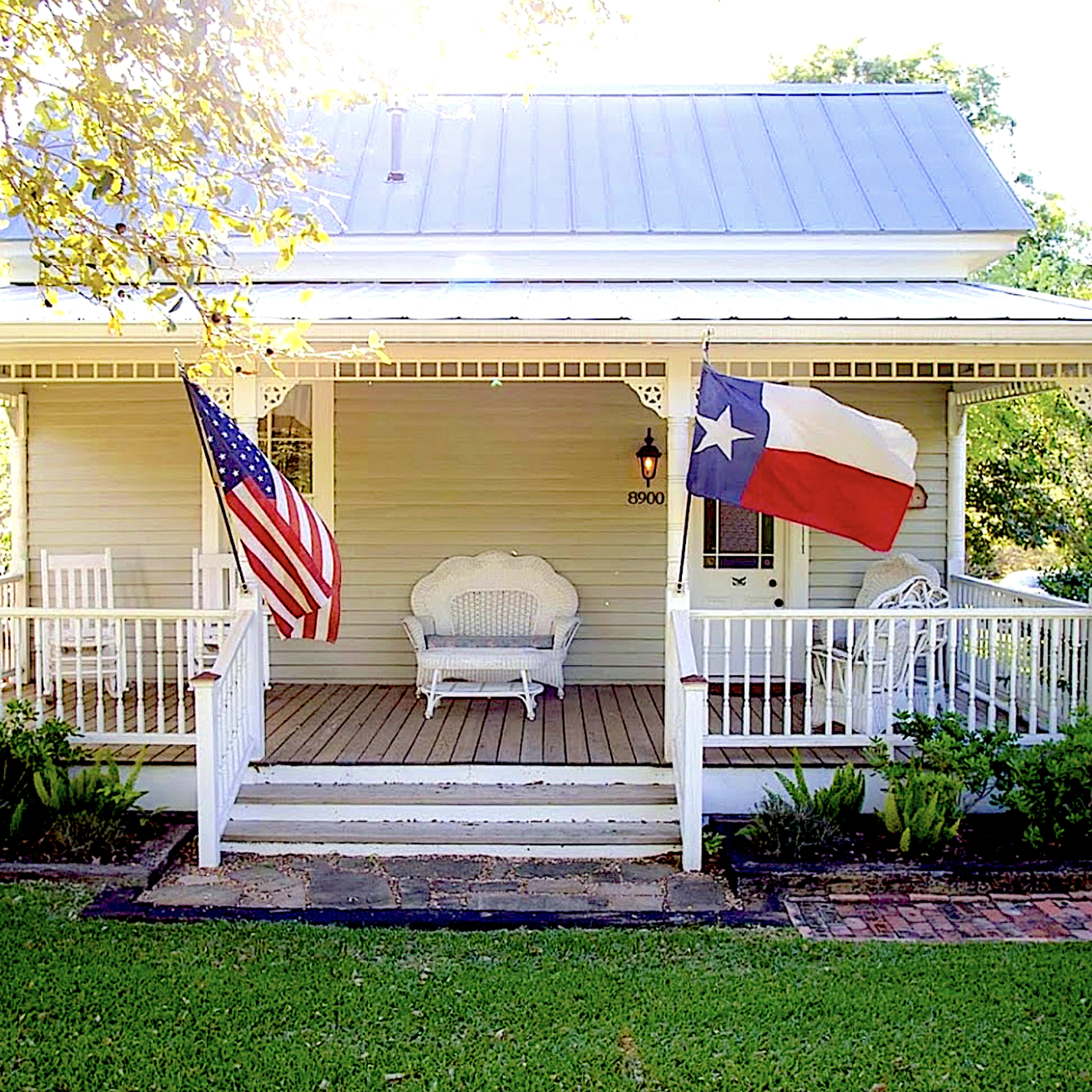 A traditional house with a front porch, featuring an American flag and a Texas flag displayed on opposite sides.