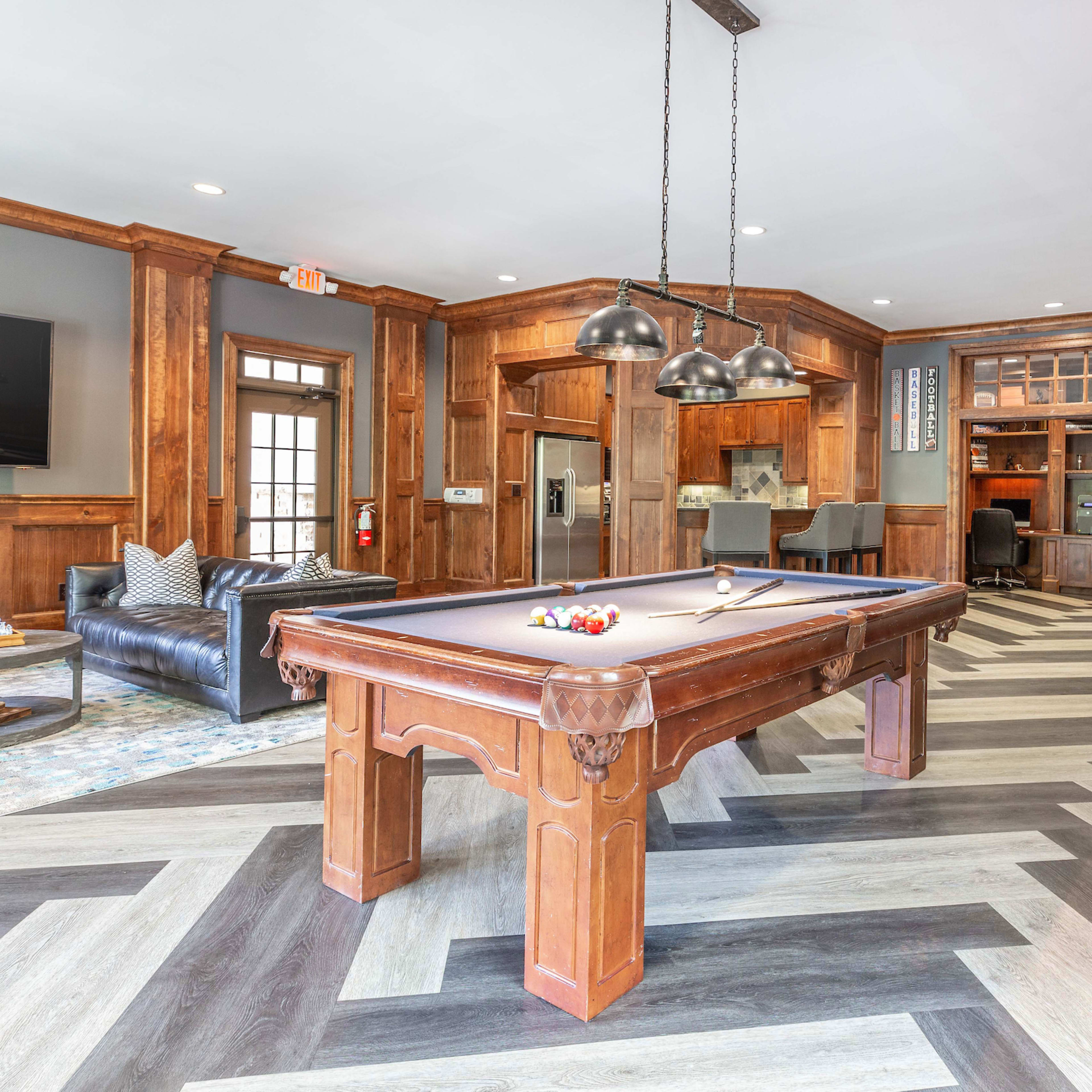 A room with a pool table, a leather sofa, and a wooden floor arranged in a herringbone pattern.