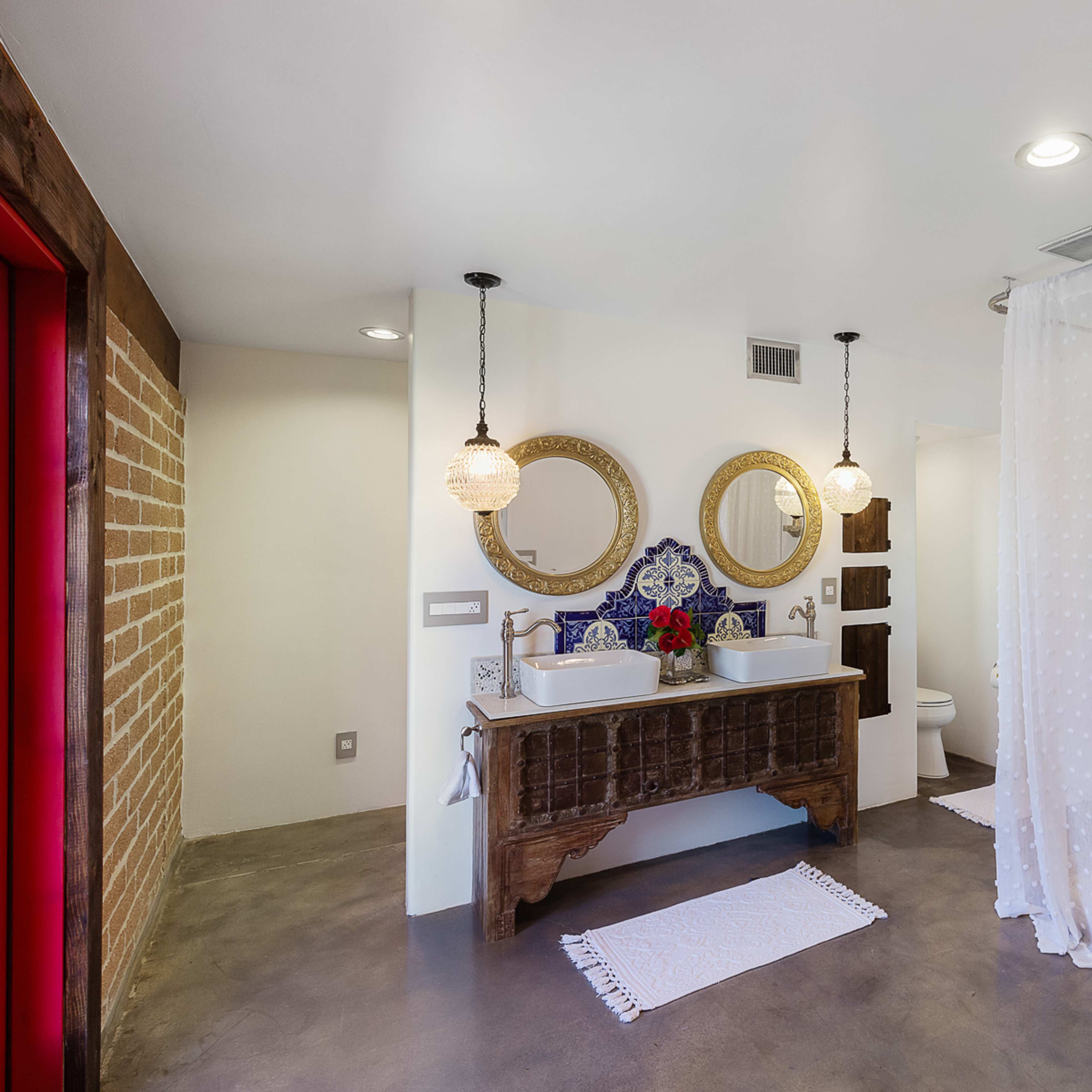 The bathroom features a wooden vanity with two sinks, circular mirrors above, a walk-in shower with tiled walls, and decorative pendant lights.