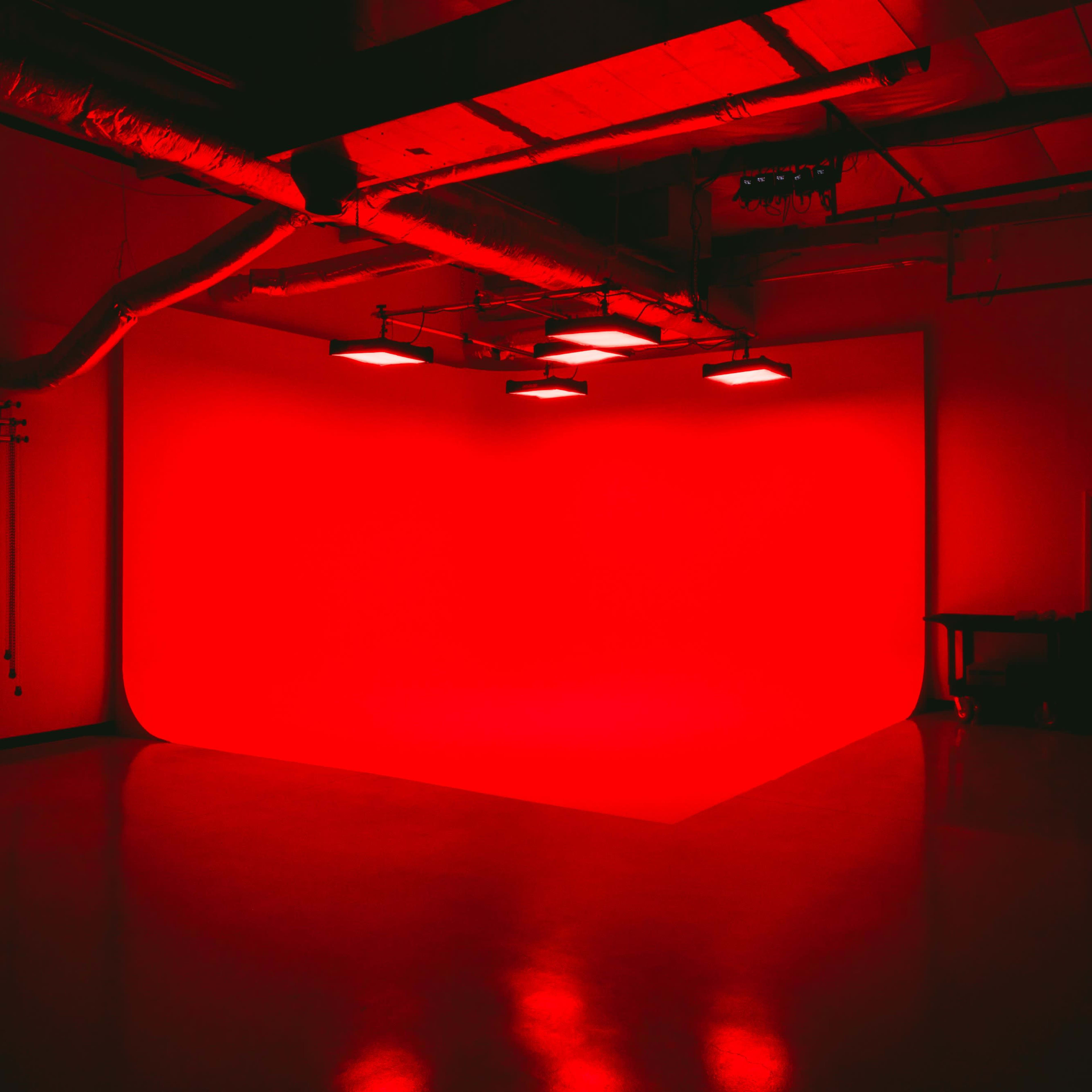 A dimly lit studio features a bright red backdrop illuminated by overhead lights.