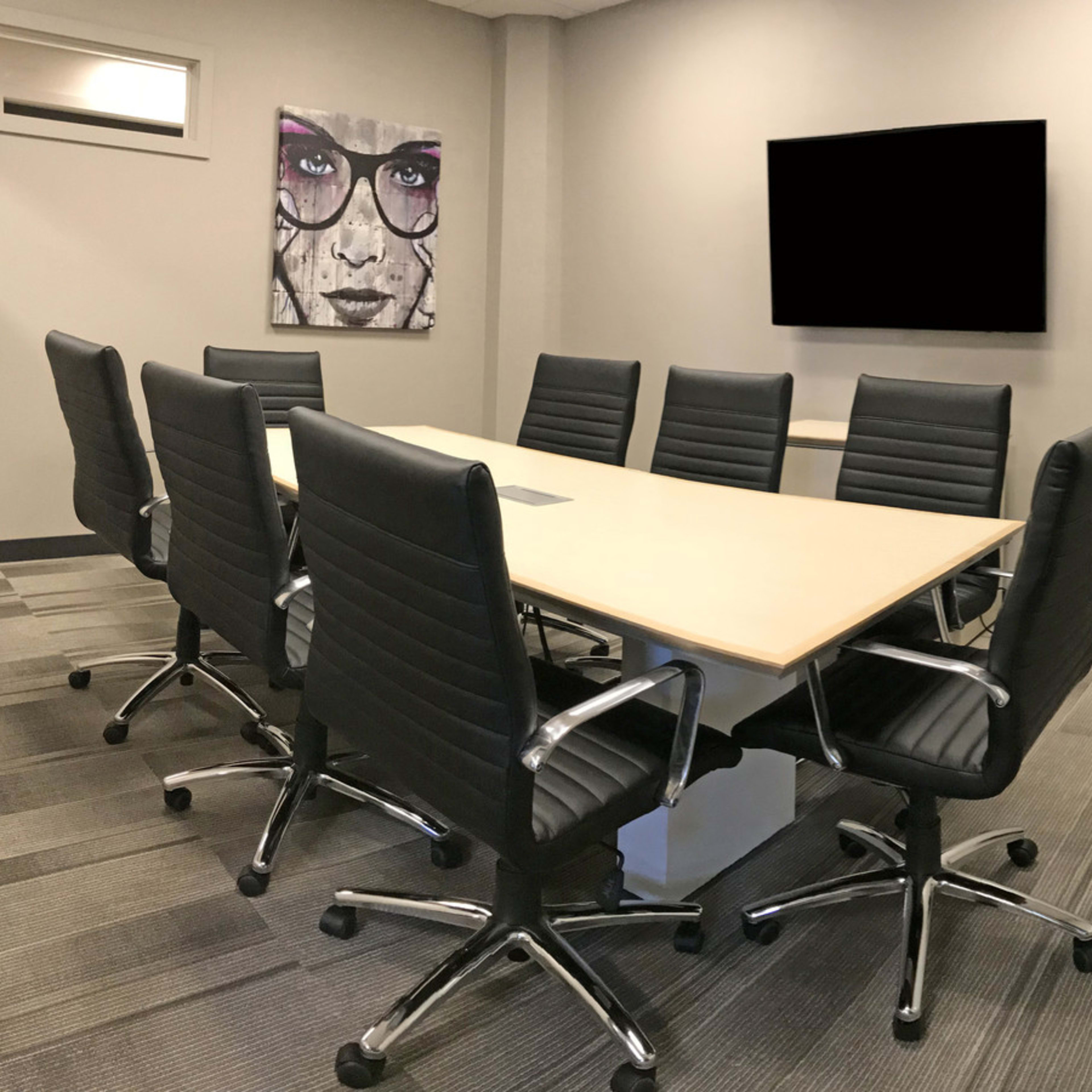 A modern conference room with a large table surrounded by black office chairs, a television on the wall, and a decorative plant in the corner.