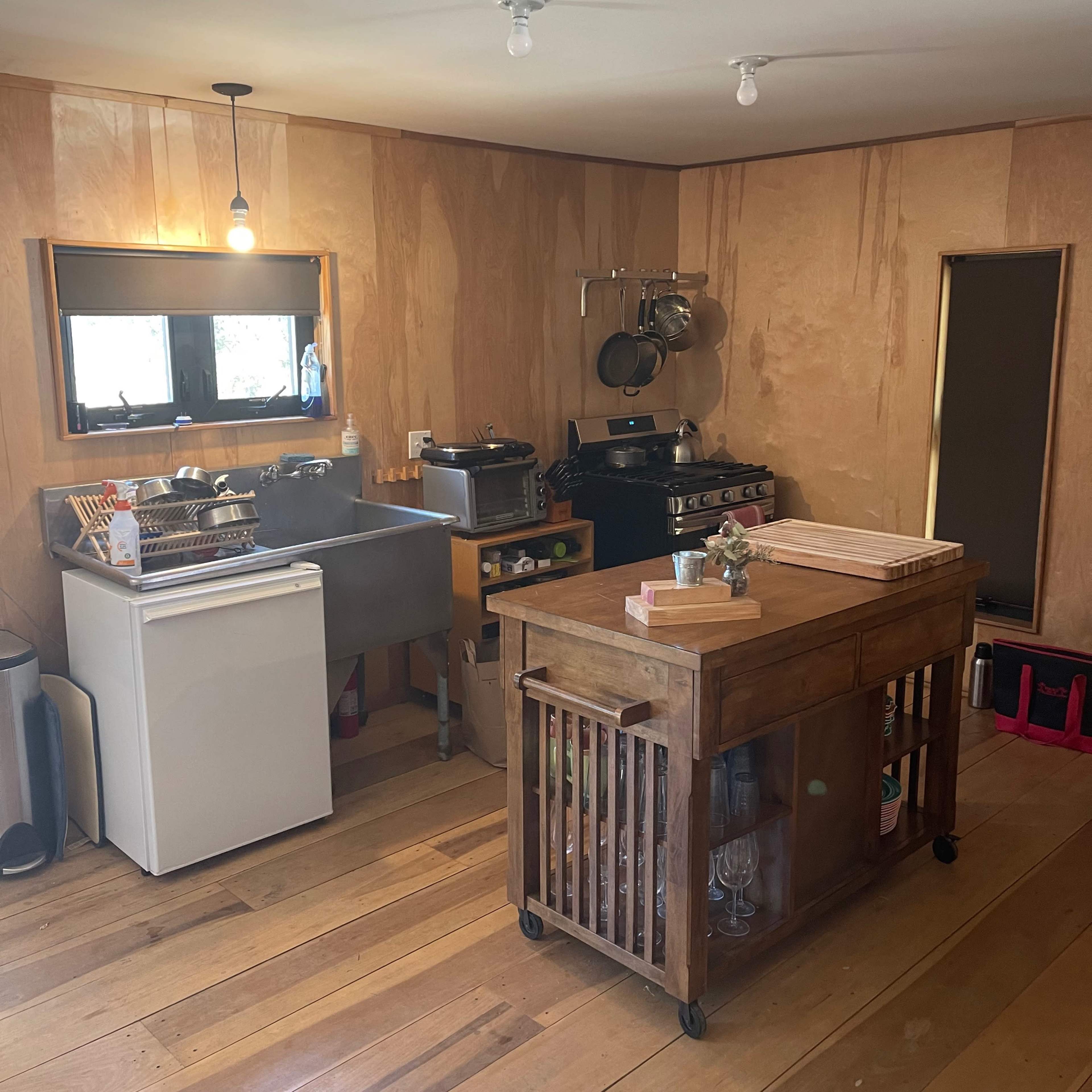 A minimalist kitchen with wooden walls, a large sink, a stove, and a central wooden cart for food preparation.