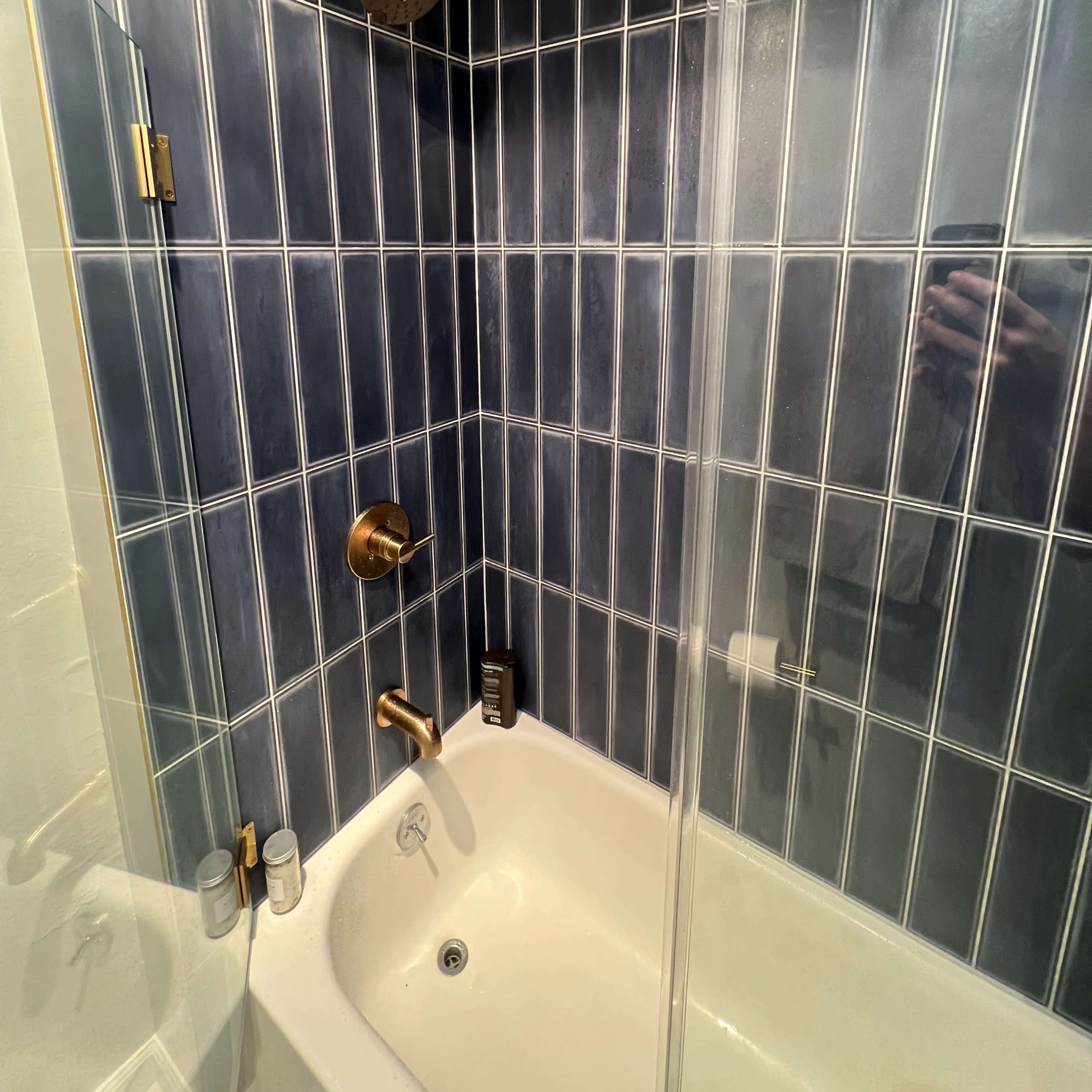 A bathroom corner with a shower enclosed by glass panels, featuring dark blue tiled walls and brass fixtures.